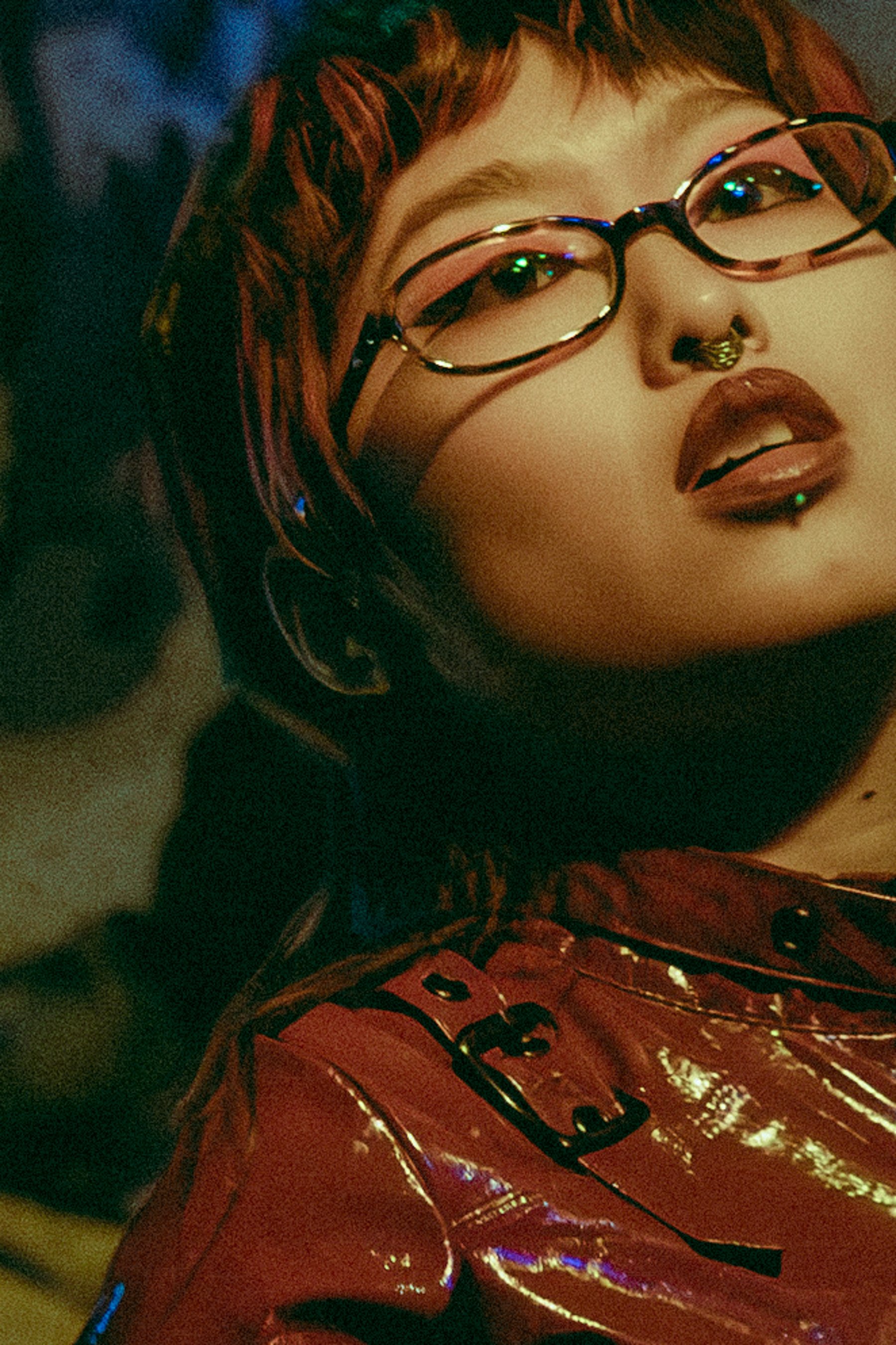 A close up of a woman with red hair and glasses, wearing a shiny red jacket, performing on stage.