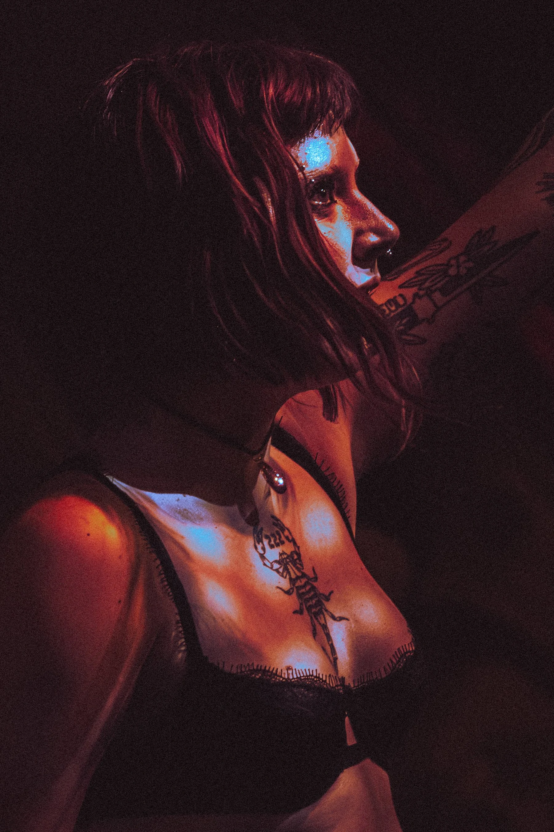 A close-up profile of a singer with dark hair and tattoos, illuminated by red and blue lighting.