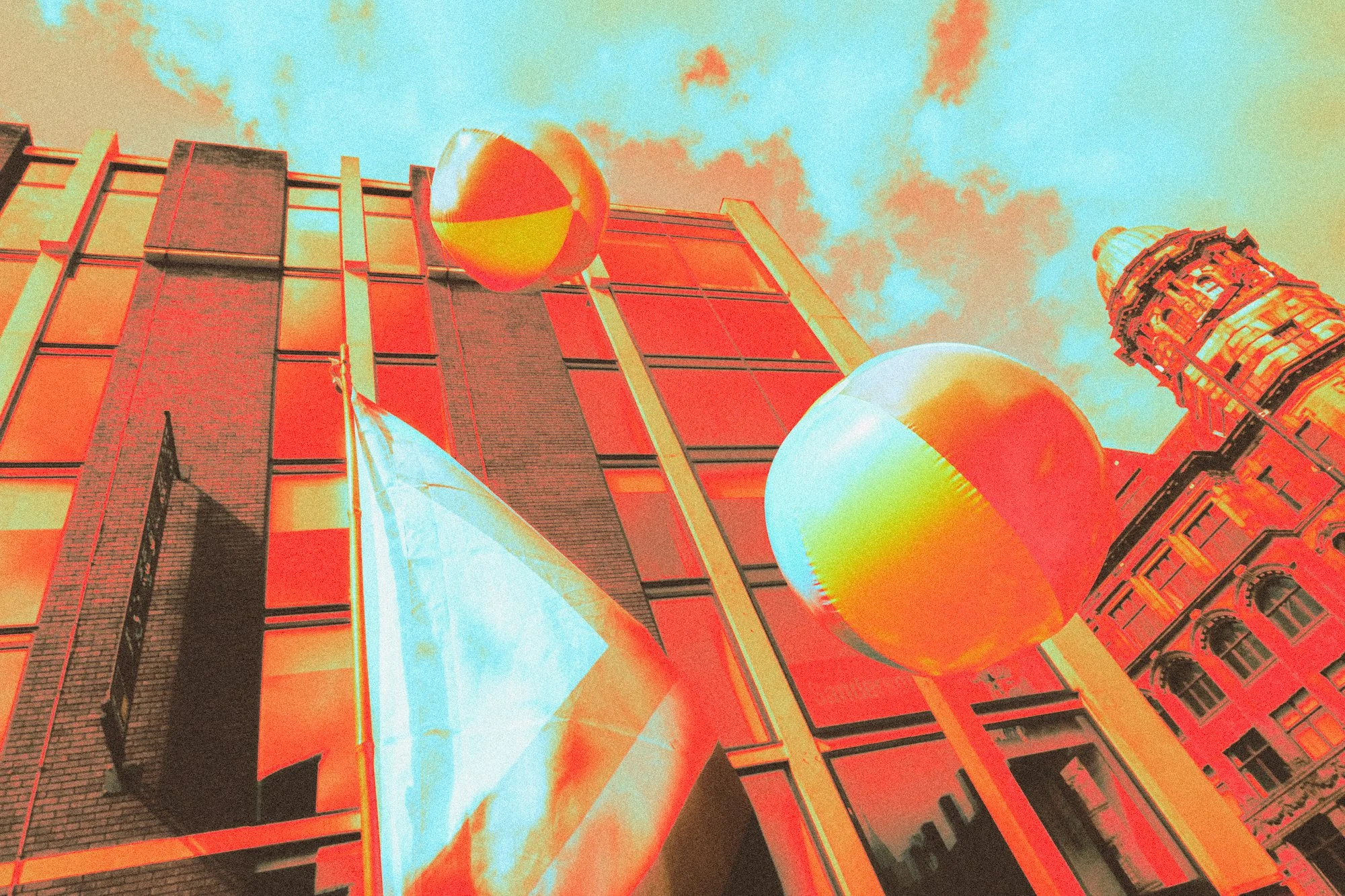 View of a building façade with spherical sculptures and a clock tower, all with an infrared or thermal imaging effect.