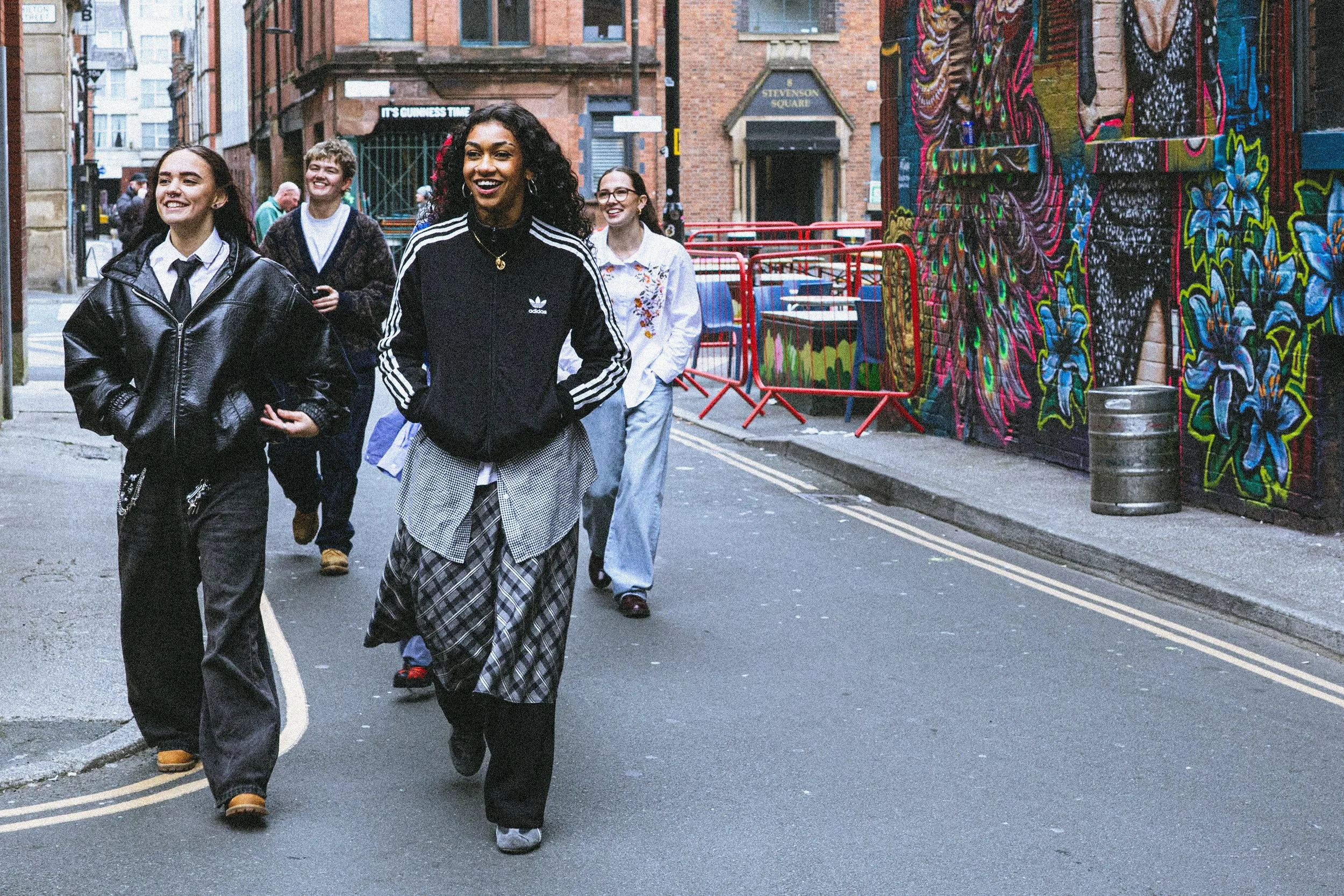 A group of young people walking down a city street with graffiti art on the walls, smiling and enjoying themselves.