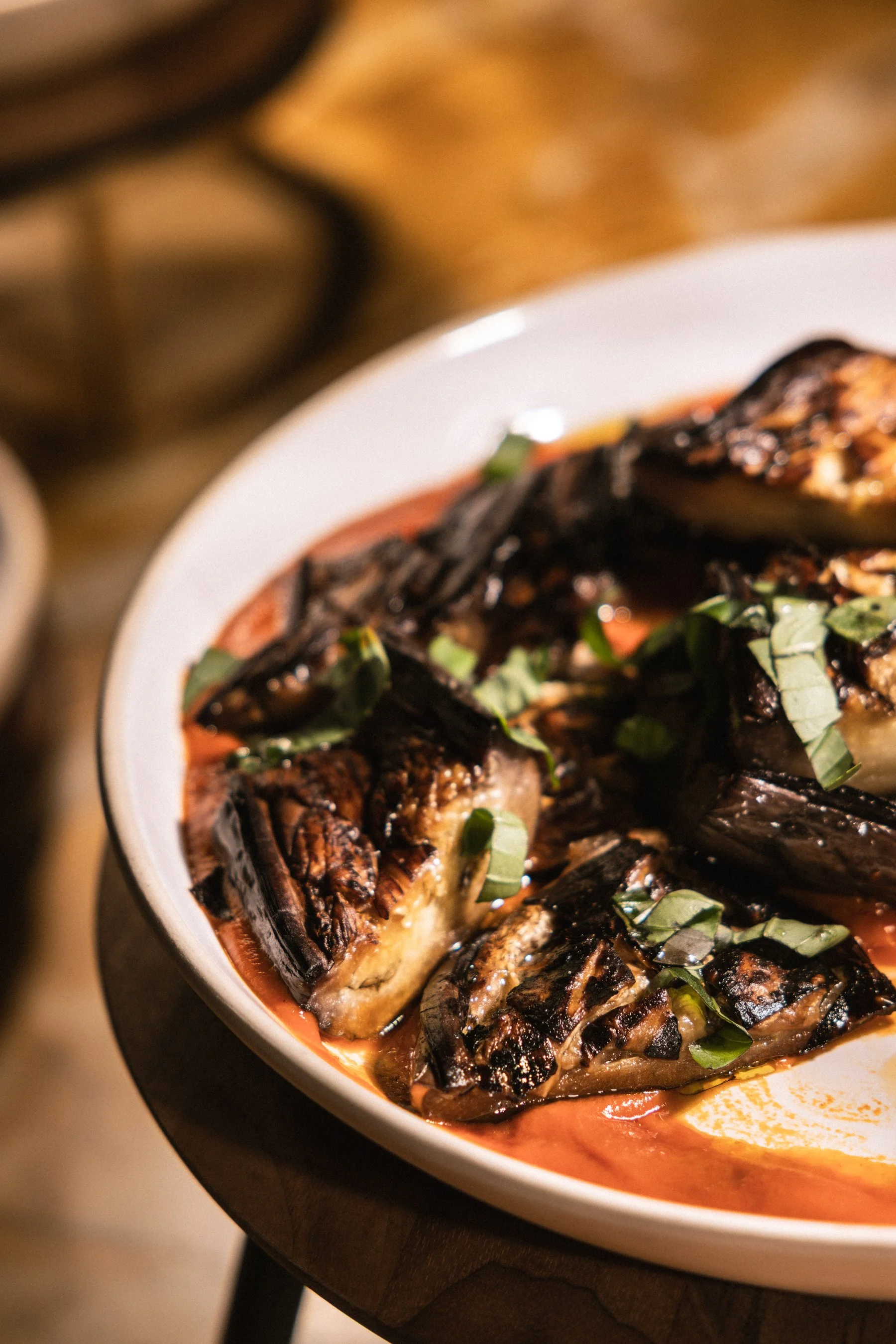 Close-up of a baked dish with roasted eggplants, herbs, and sauce in a white bowl.