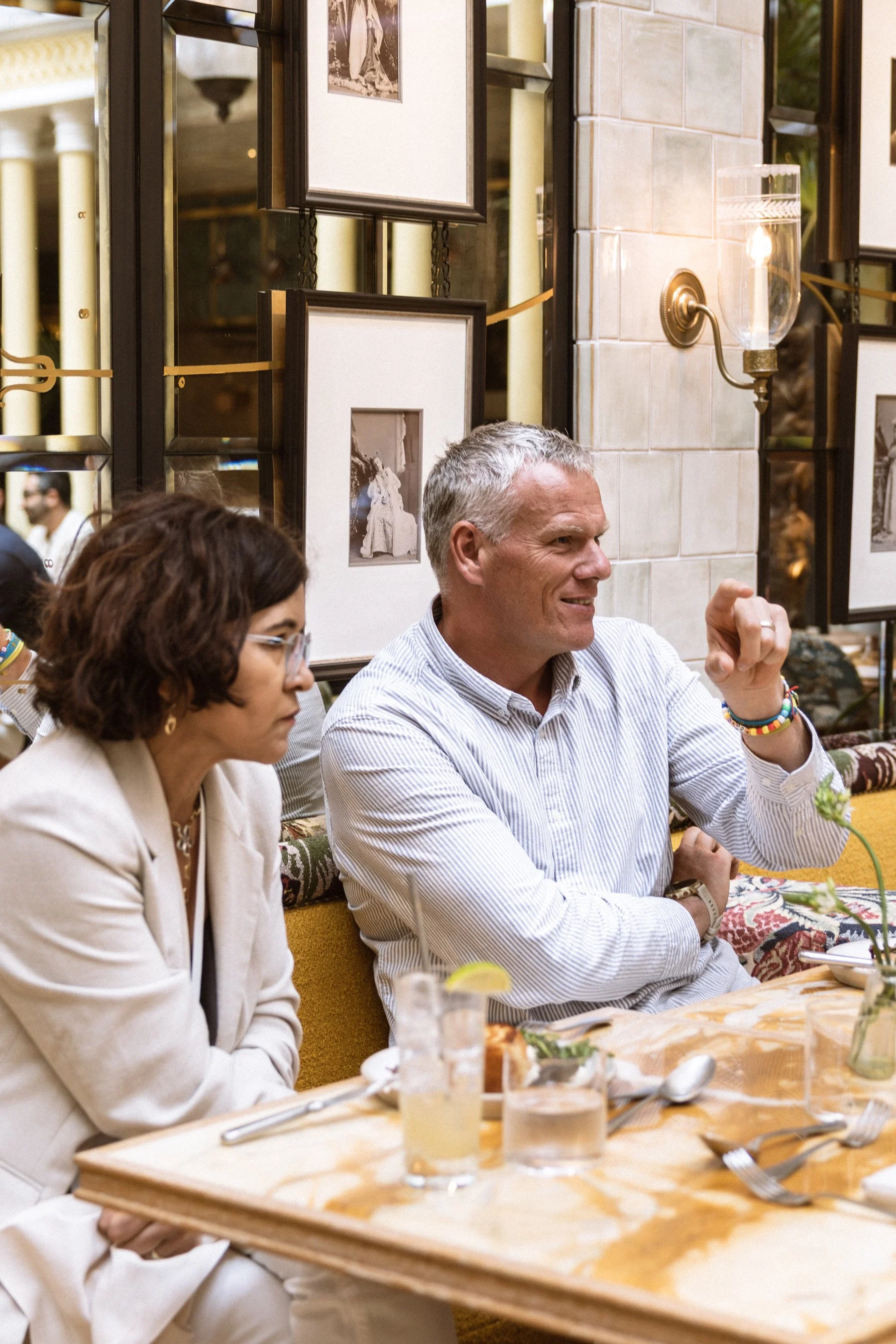 People sitting at a dining table in a restaurant or cafe, with framed photos on the wall and a wall-mounted light fixture.