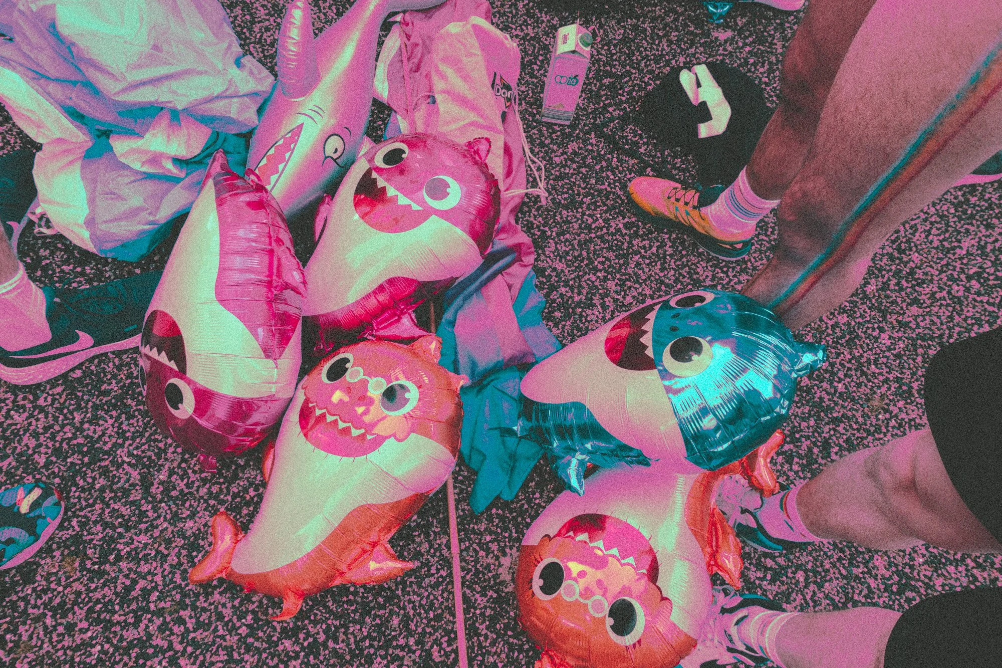 Colorful dolphin-shaped and fish-shaped balloons on a speckled floor, with someone wearing colorful sneakers and striped socks.