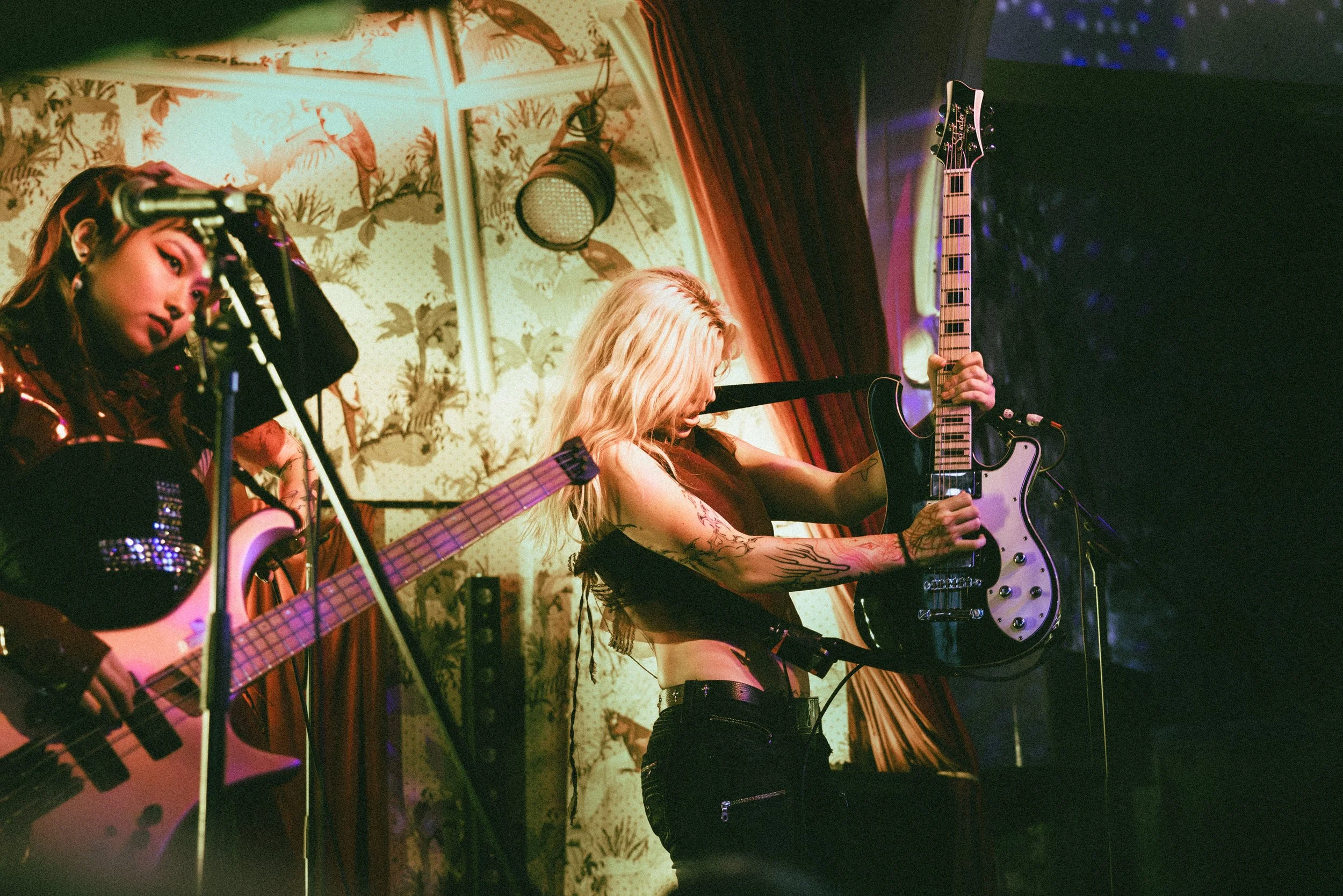 Two live music performers on stage - both playing electric guitars.