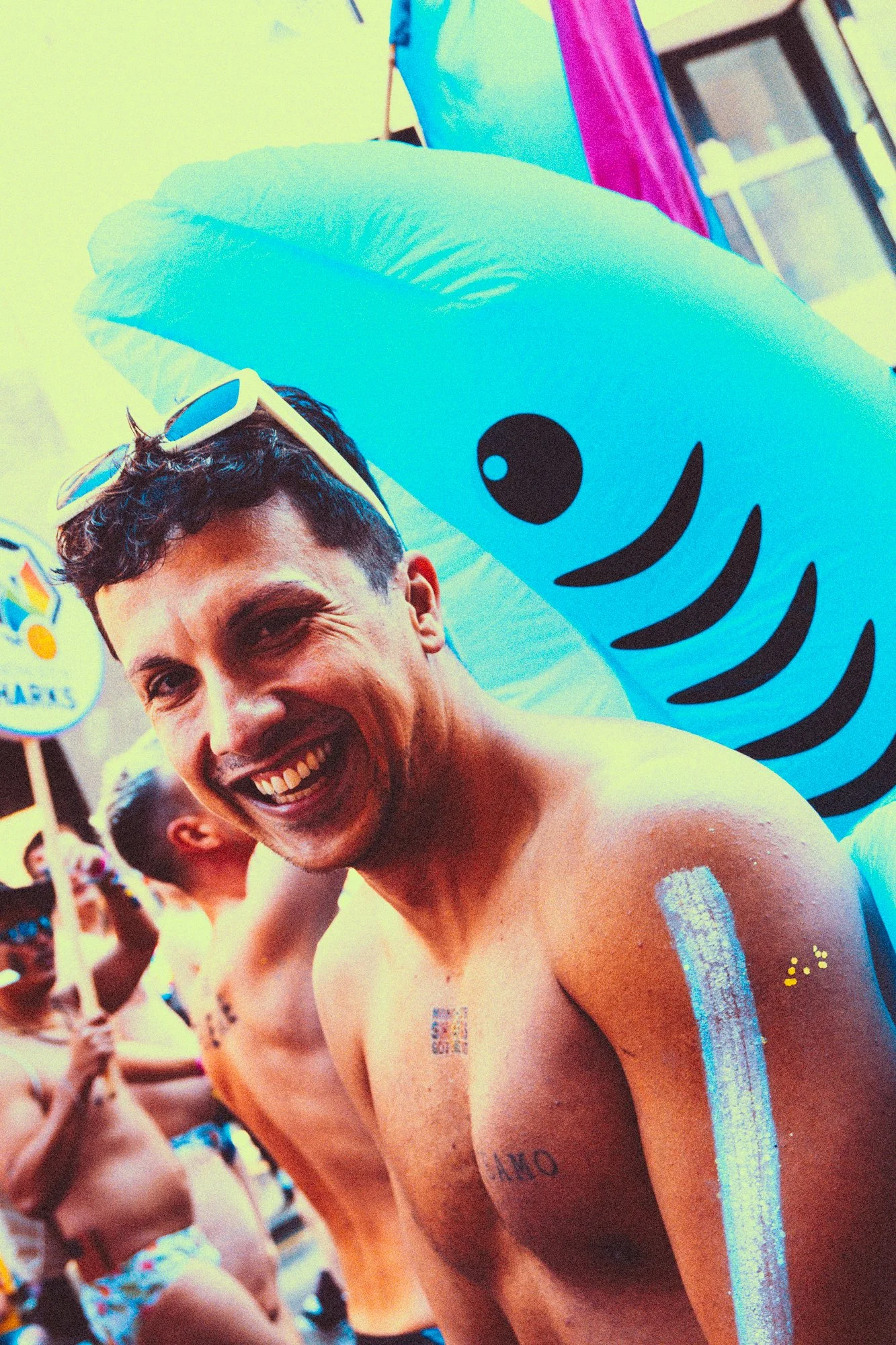 A group of young men participating in a colorful outdoor event, smiling and with glowing body paint and shark costumes.