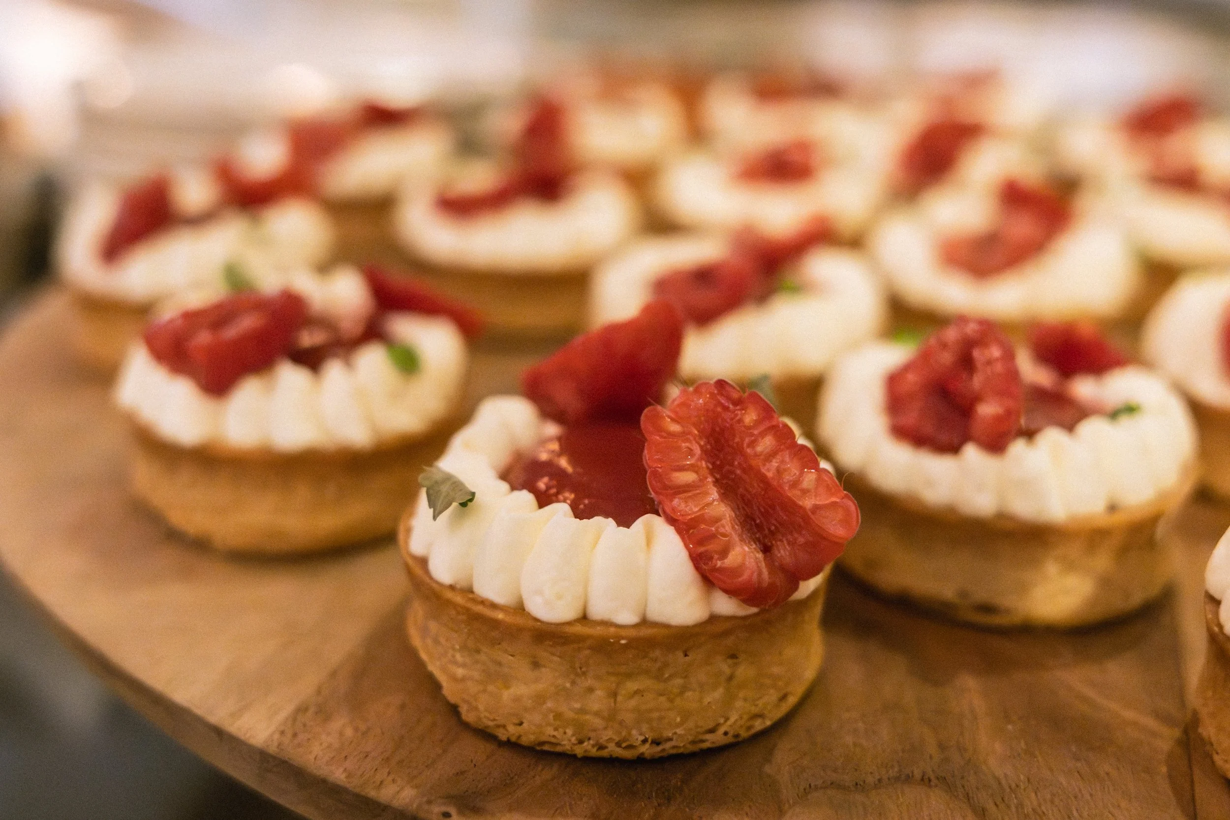 Close-up of small tartlets topped with cream and strawberries on a wooden surface.