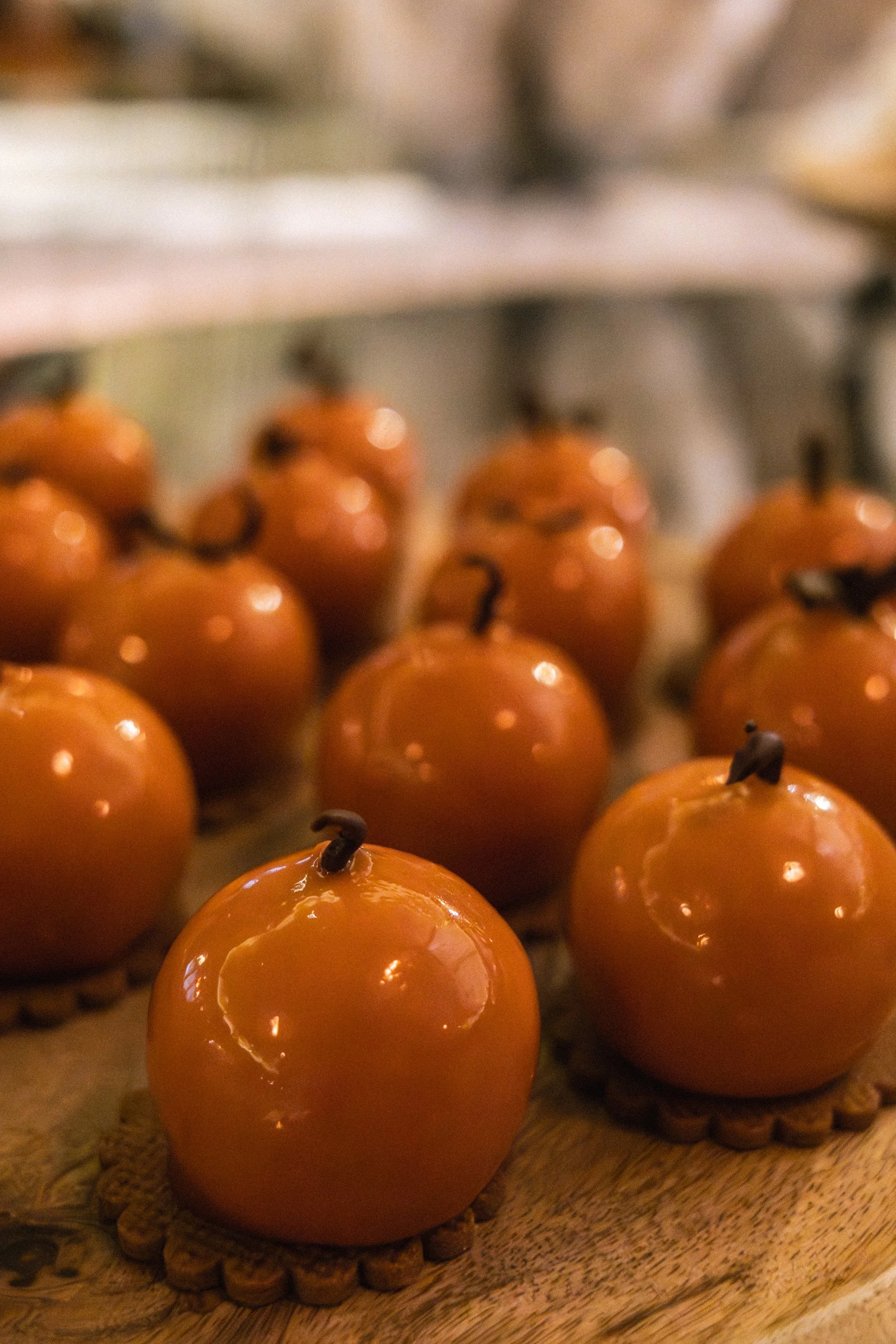 Close-up of small, round, glossy orange candies with chocolate chips on top, arranged on a wooden surface with a woven mat underneath.