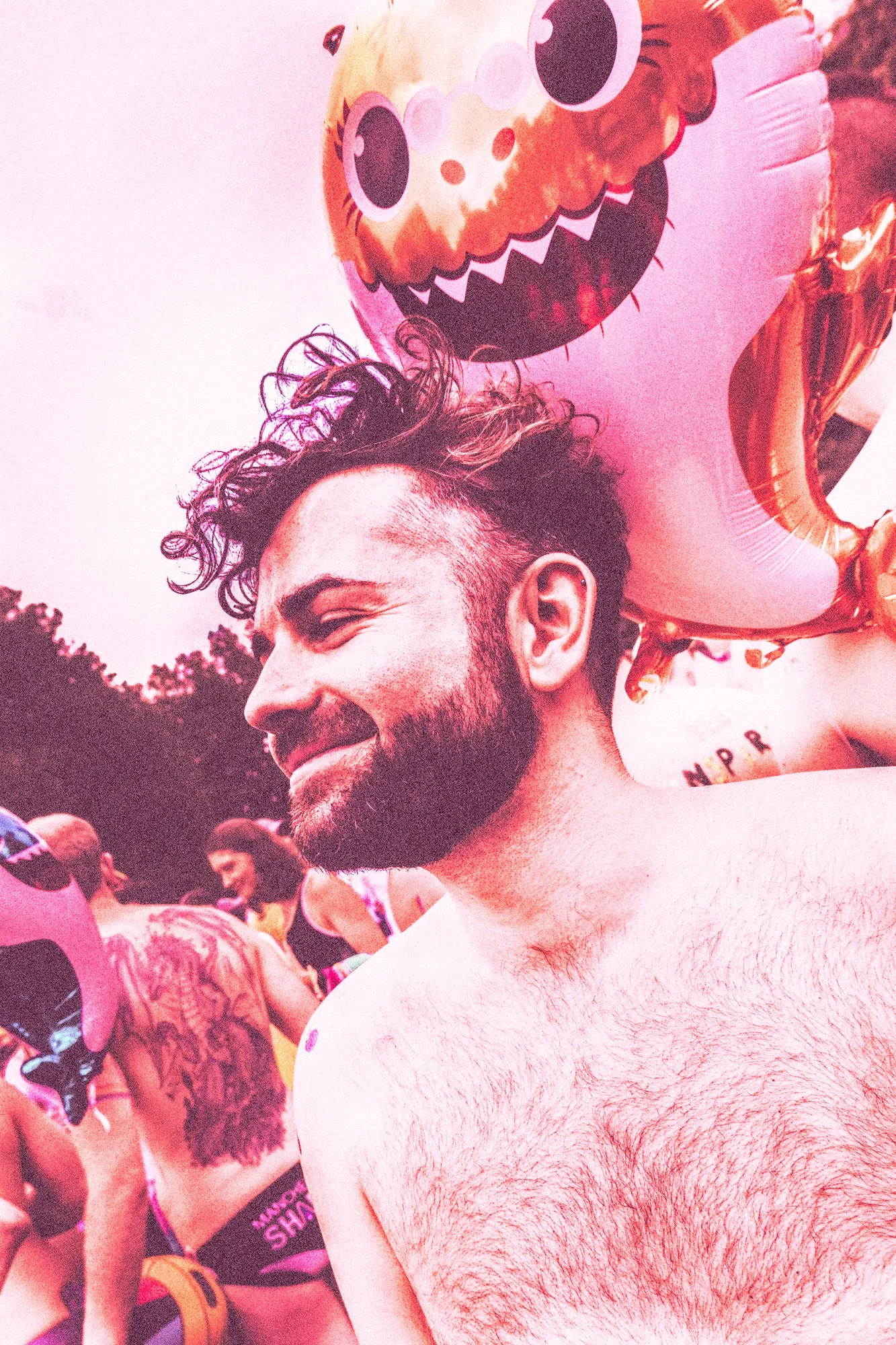 A man with curly hair and a beard smiling at a crowded outdoor event, holding a colorful character balloon.