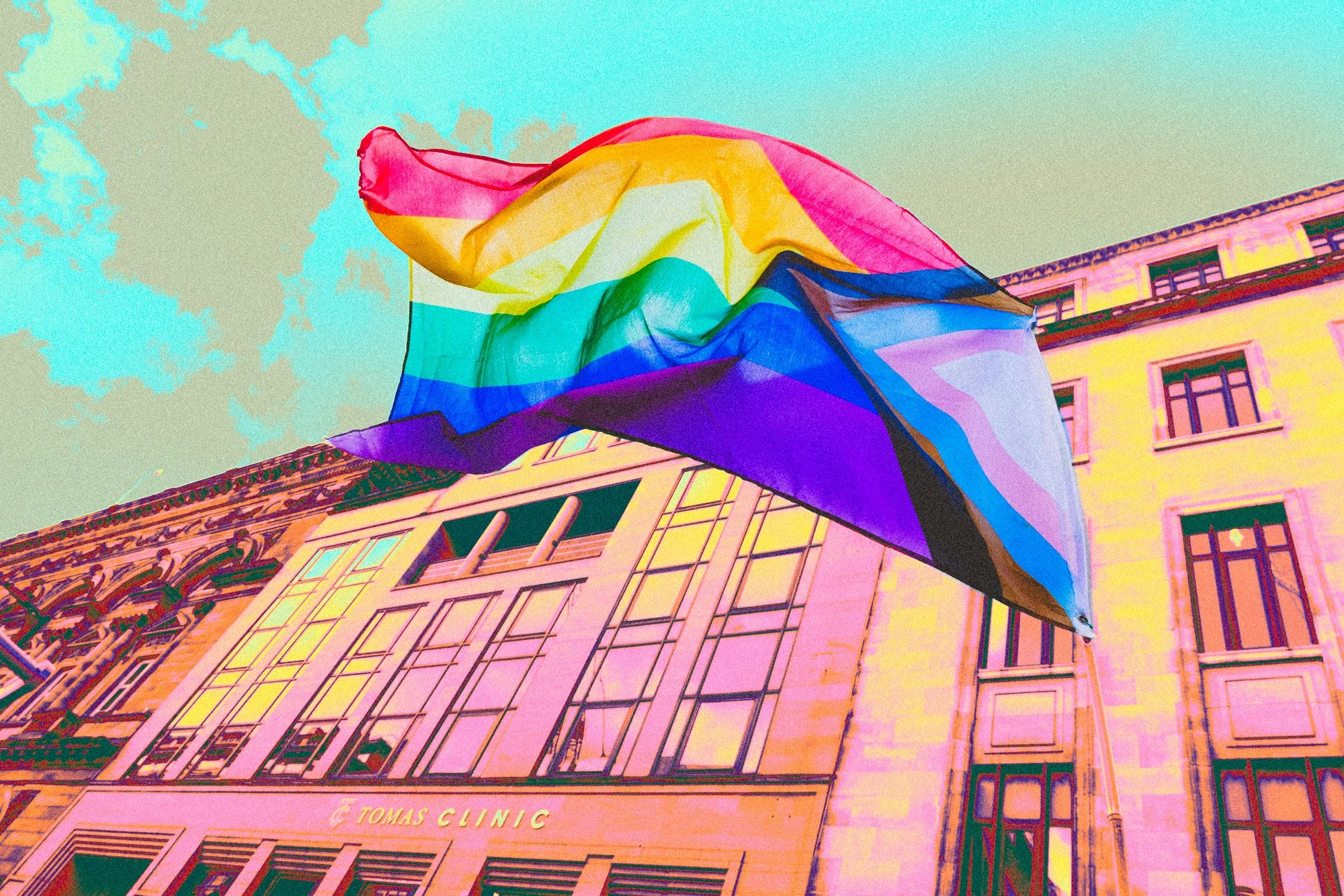 A rainbow pride flag flying outside a building with ornate architectural detailing and signs that read 'Tomas Clinical'.