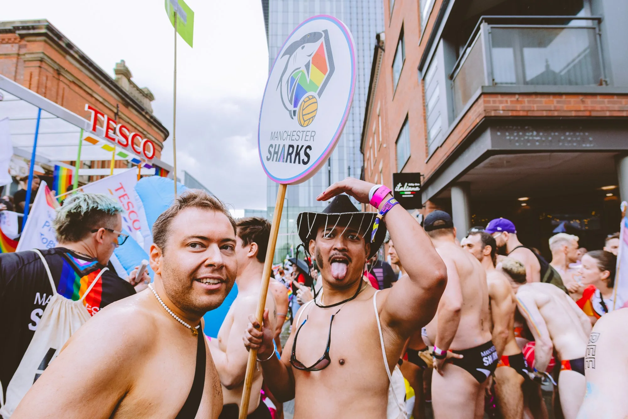 People attending a pride parade in Manchester, celebrating LGBTQ+ pride, with rainbow flags and supportive signs, amidst a city street scene.