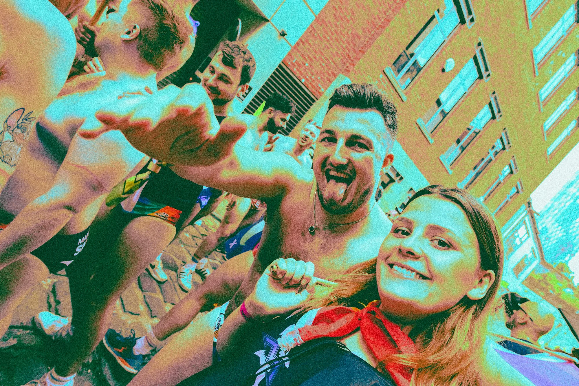 A group of young people, some in athletic wear, are excited and smiling, taking a selfie outdoors with a building in the background.