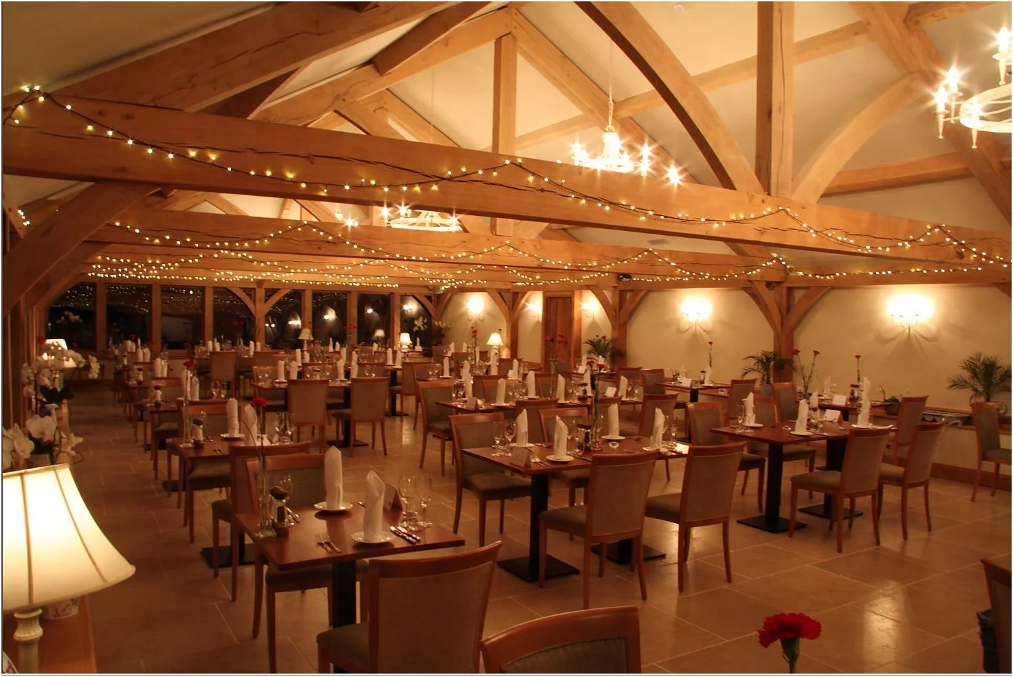 Elegant indoor private hire room decorated with string fairy lights, wooden beams, and tables set with white napkins, glasses, and flowers.
