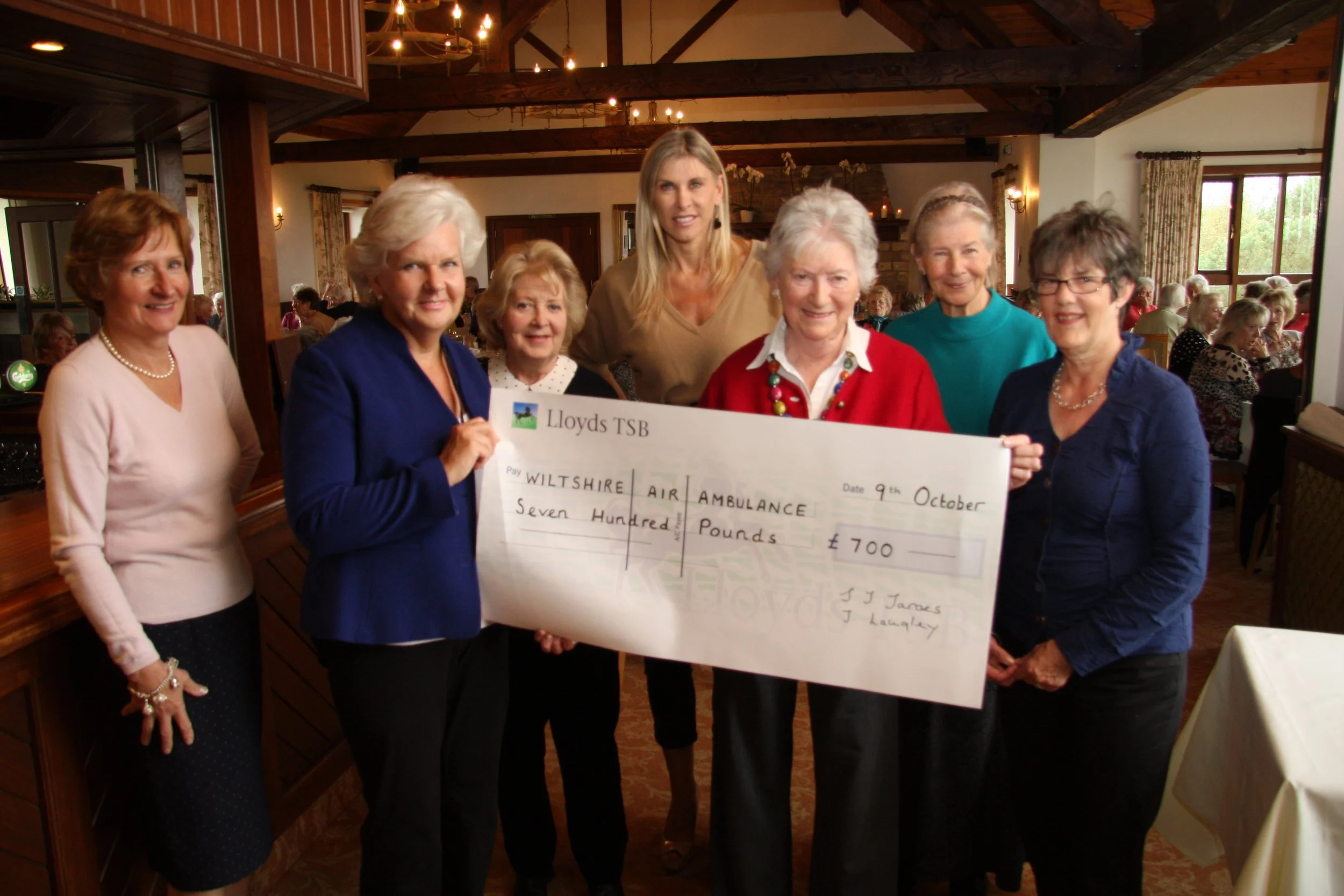 Group of people holding a large cheque for charity at a gathering in a decorated room.