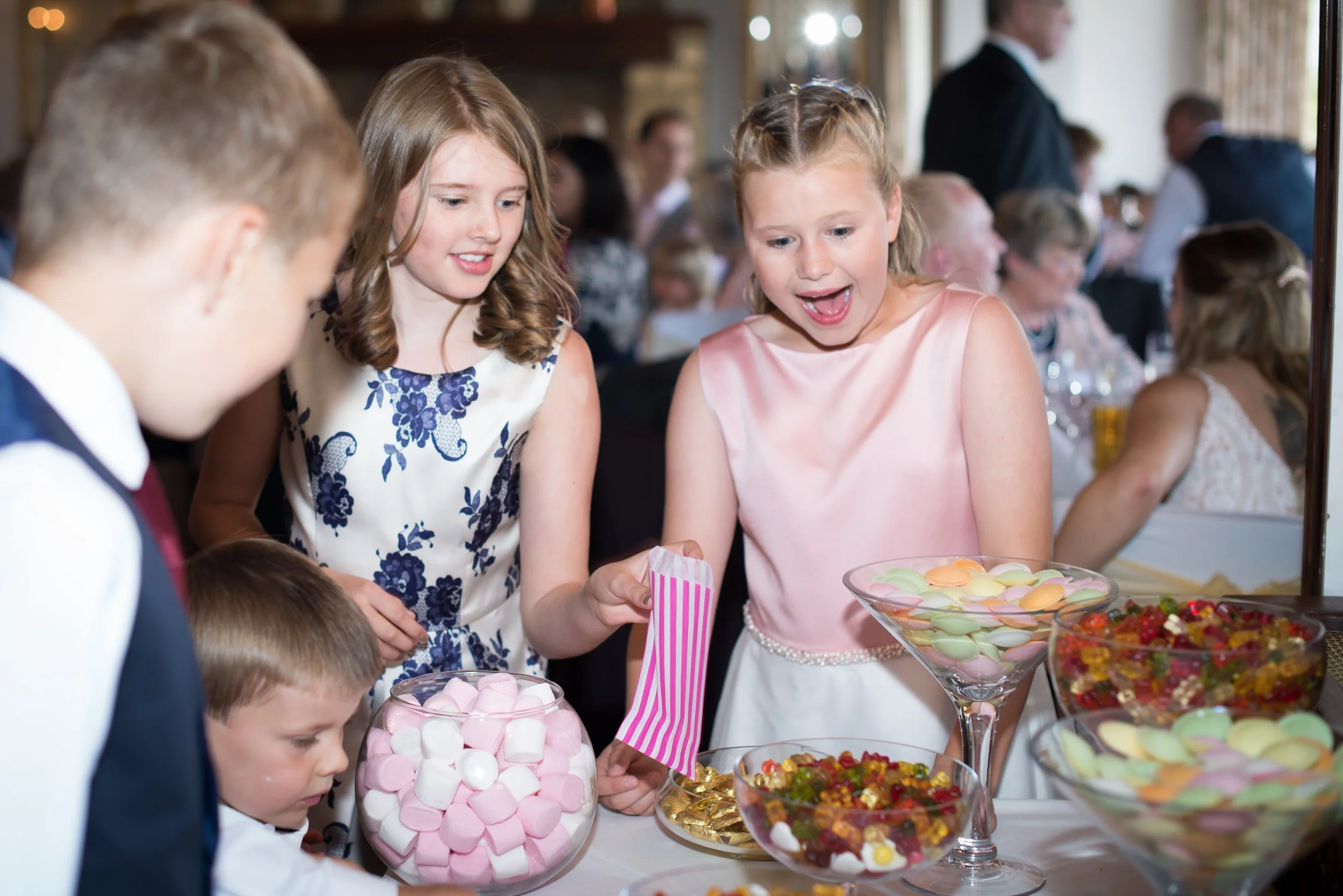 Children at a party looking at colorful candies and desserts on a table.
