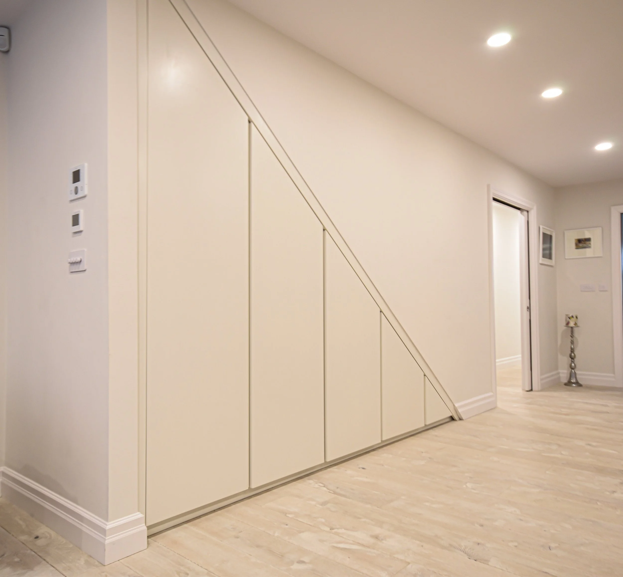 Interior hallway with built-in under-stair storage cabinets, light wood flooring, and recessed lighting.
