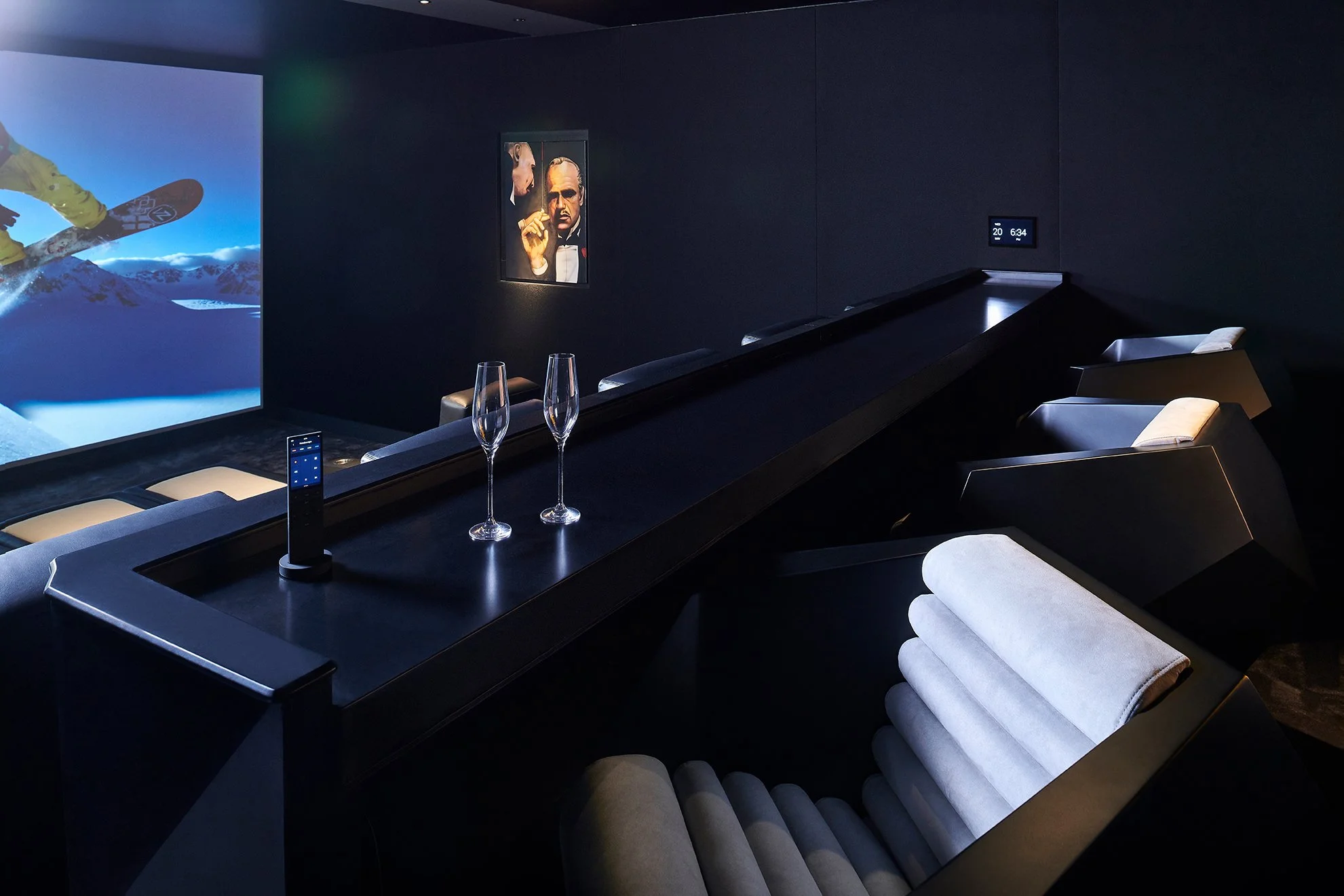 Home theater with recliner seats, remote control, two glasses, large screen showing a snowboarder, and movie poster on the wall.