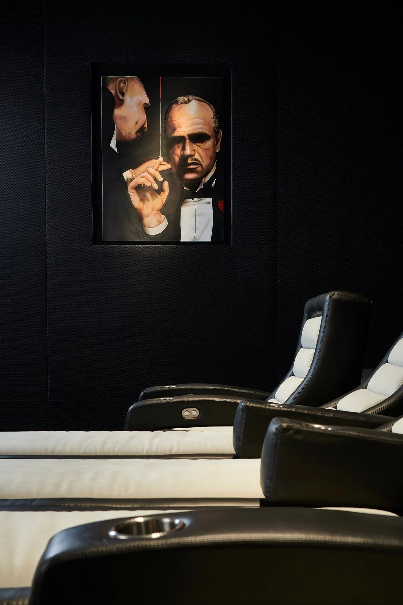Modern black and white home theater with luxury recliner seats and a framed painting of a classic movie scene on a dark wall.