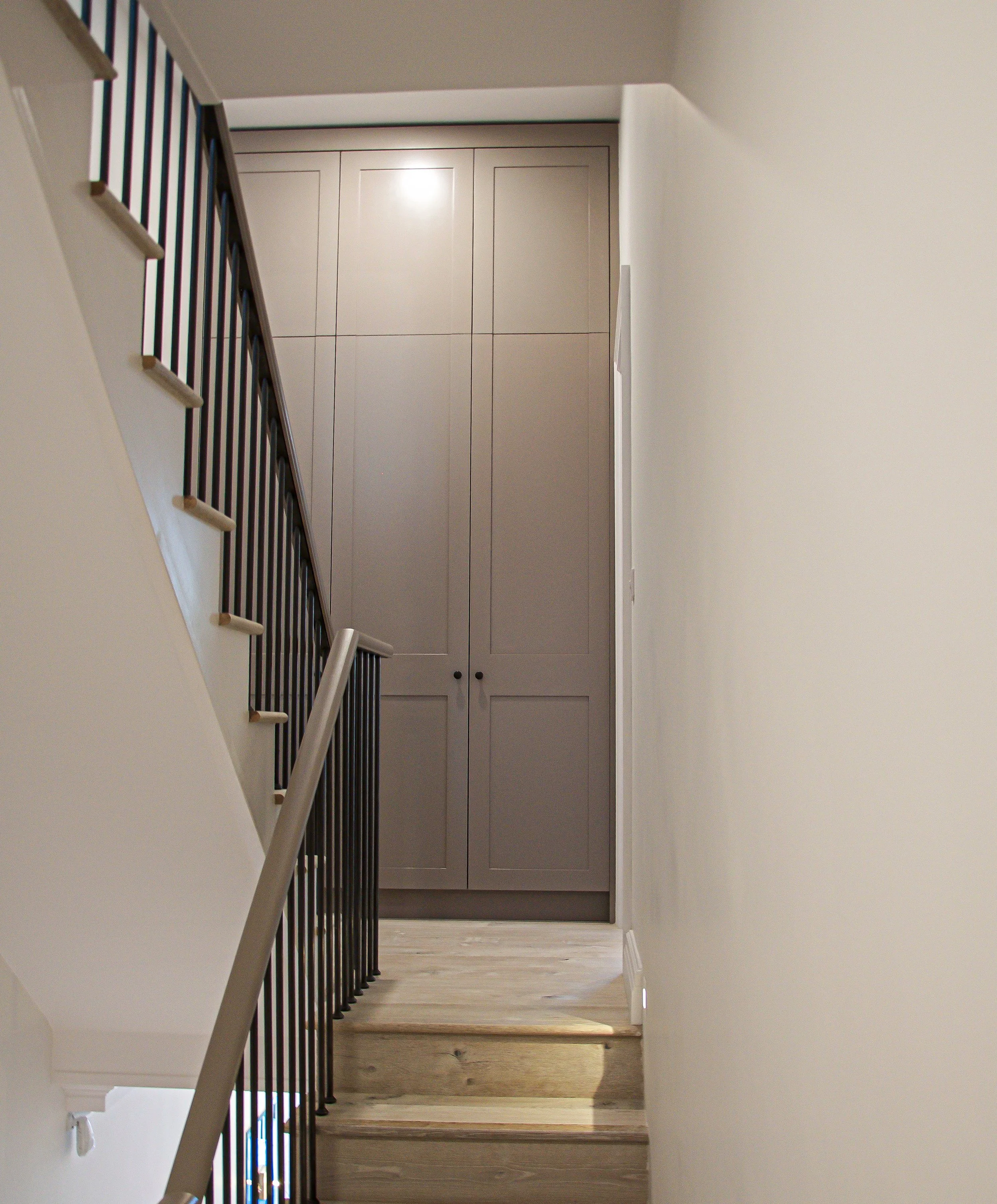 Interior staircase with wooden steps and metal railing leading to a closed closet with double doors at the top landing.