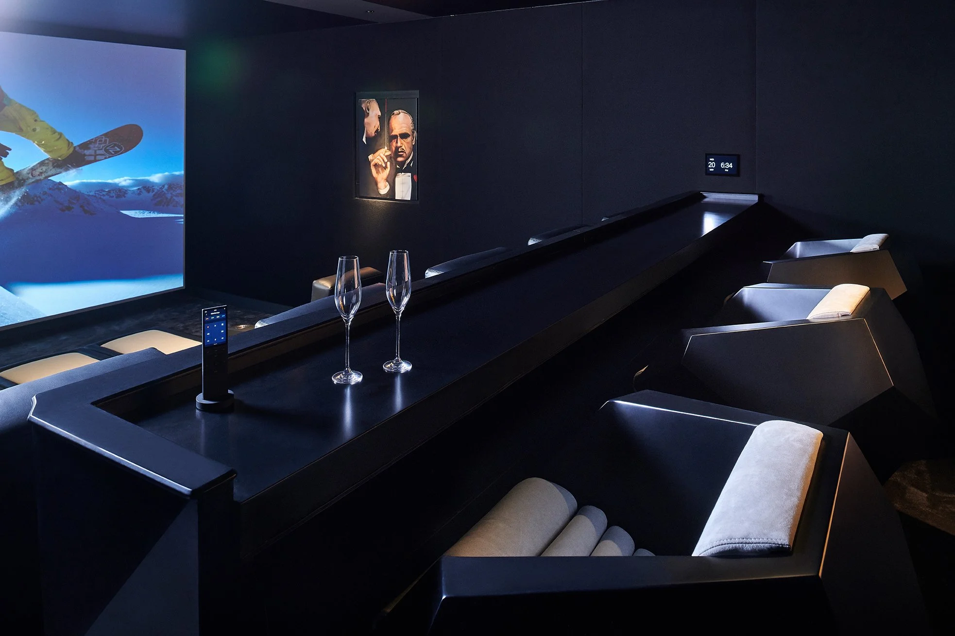 Luxury home theater with black reclining chairs, a large screen showing a snowboarding scene, two empty champagne glasses, and a wall painting. The room has a sleek, modern design.