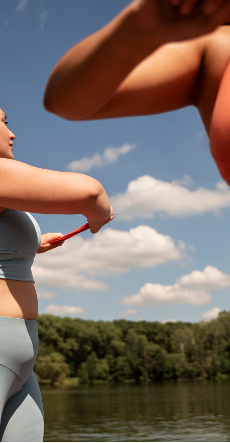 Two women in activewear stretching outdoors by a lake, enjoying movement together on a sunny day
