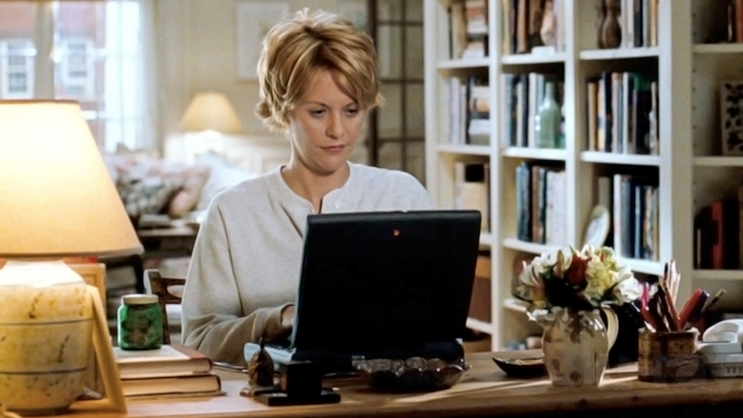 A woman sitting at a desk in her cozy home, typing on a laptop.