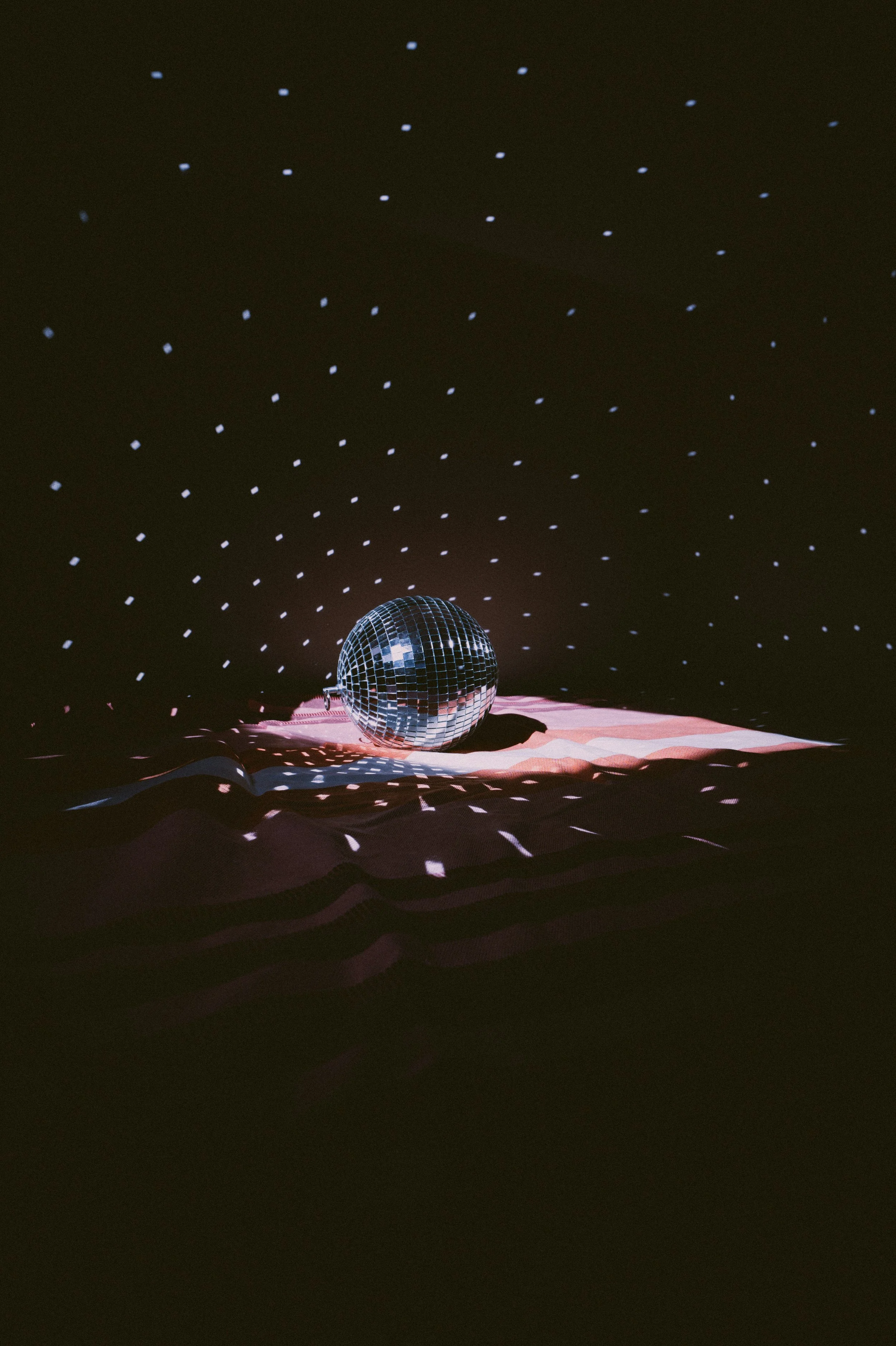 Une boule disco suspendue, projetant des lumières brillantes sur un drap rose en dessous, avec un fond sombre et de petites lumières blanches dispersées dans l'espace au-dessus.