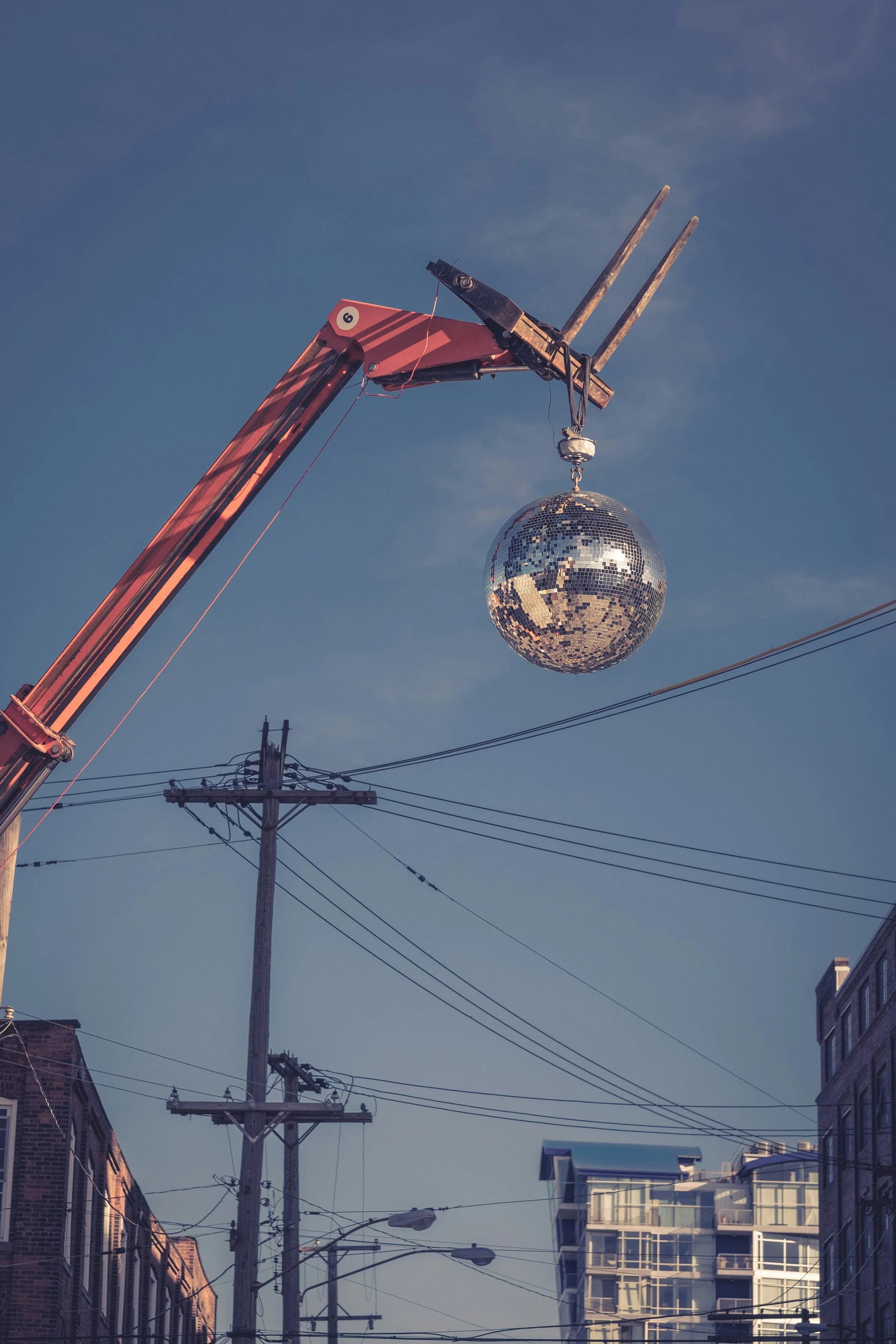 Une boule de discothèque suspendue dans le ciel au-dessus d'une rue urbaine avec des lignes électriques et des bâtiments.