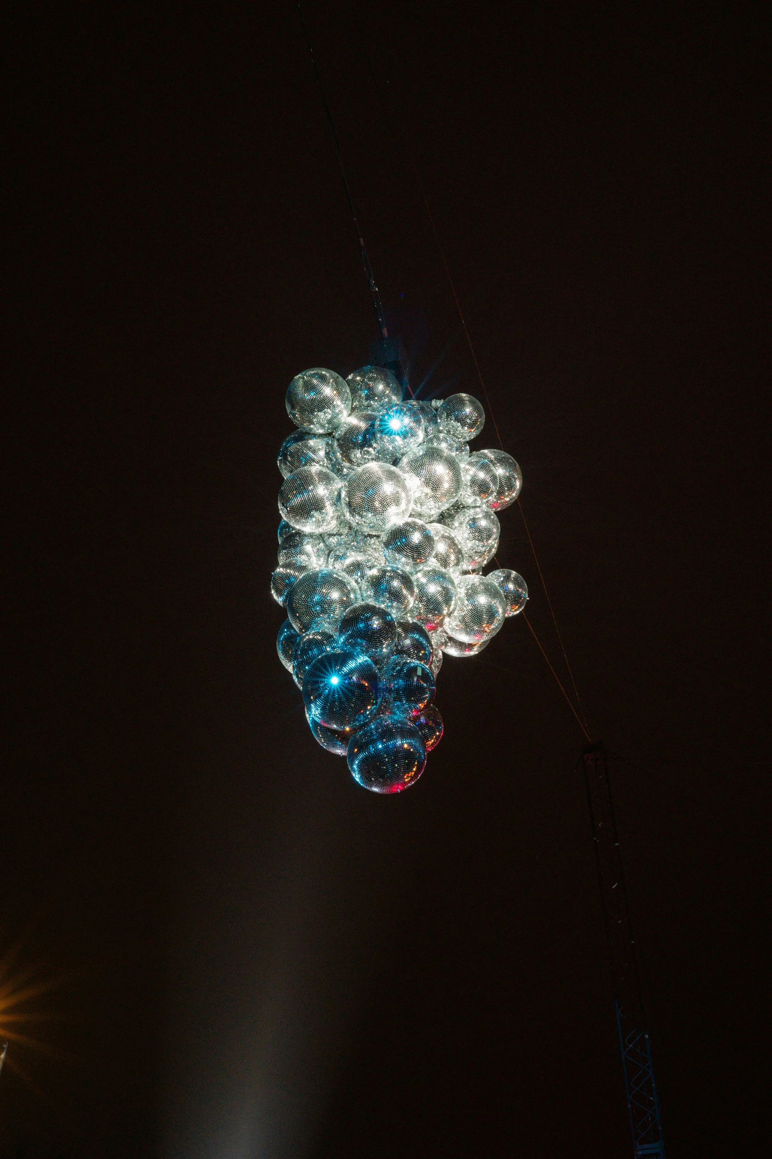 Une structure suspendue composée de nombreux miroirs en forme de boules, illuminée contre un ciel nocturne.