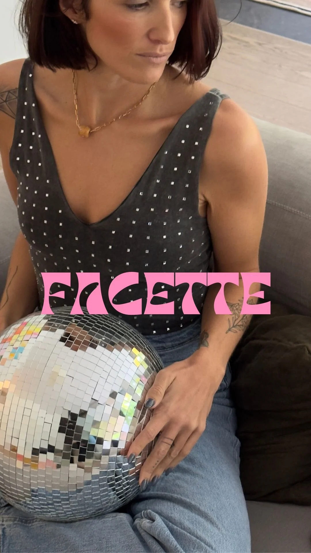 Une femme avec des tatouages, portant un haut gris à pois blancs, tenant une boule de disco