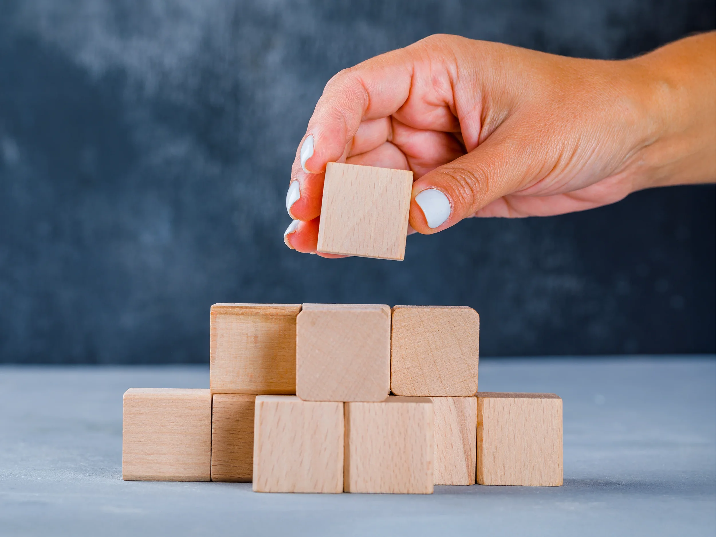 Hand placing a wooden block onto a growing stack of blocks, symbolizing the stages of company growth, business development, and building a strong operational foundation.