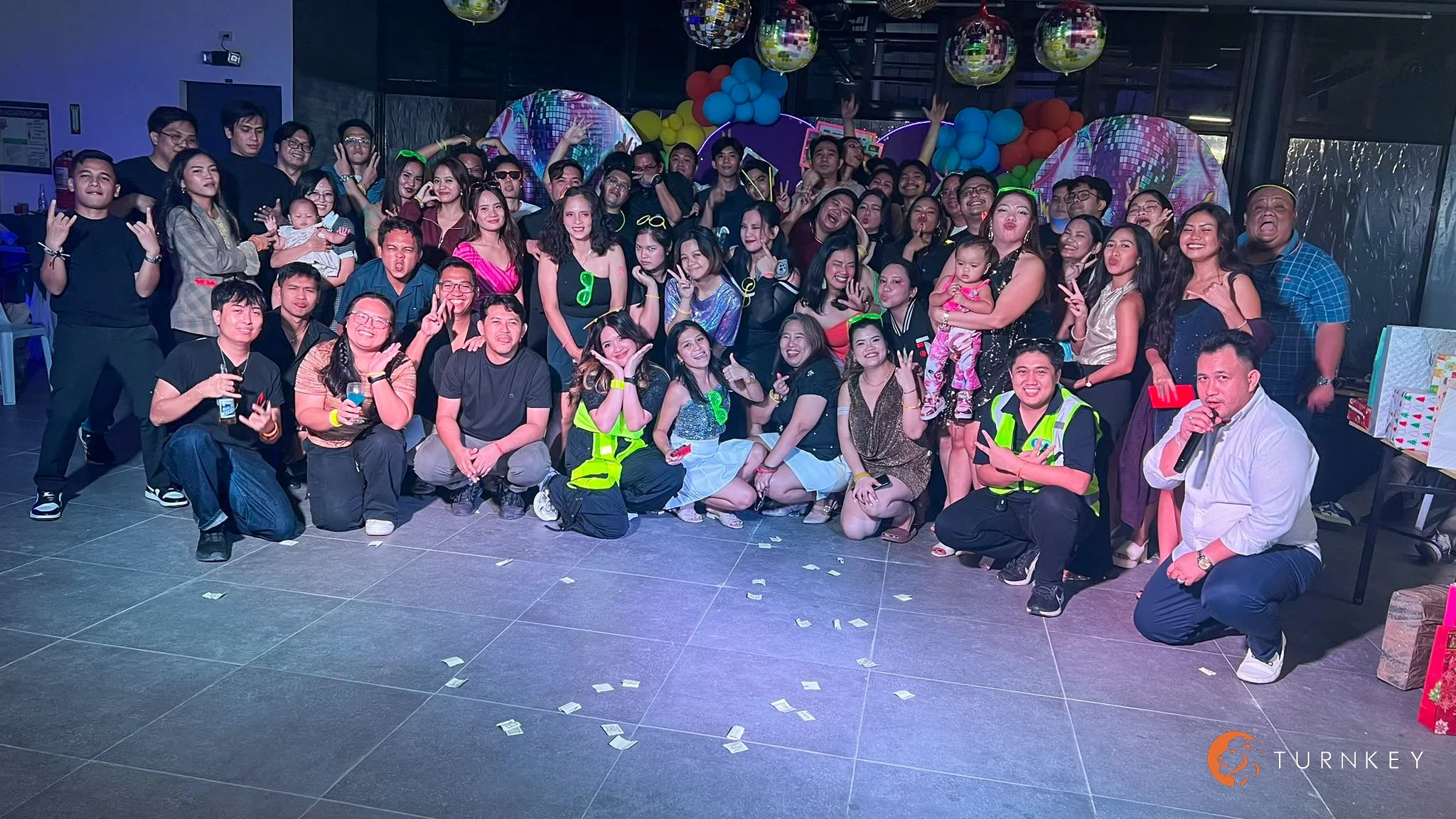 Group photo of our offshore team during the 2025 year-end party, with employees posing together on a decorated event floor surrounded by colorful balloons, disco balls, and party lights
