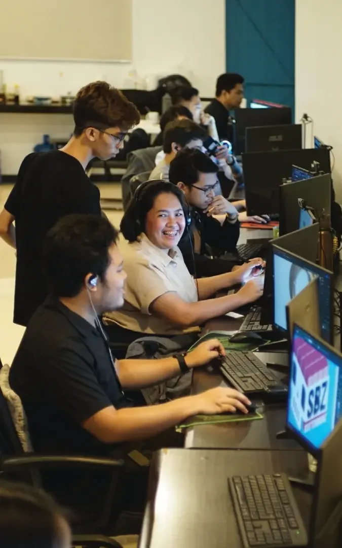 Offshore team members working together at computer stations in a modern office, collaborating on tasks while wearing headsets and monitoring multiple screens in a fast-paced work environment.