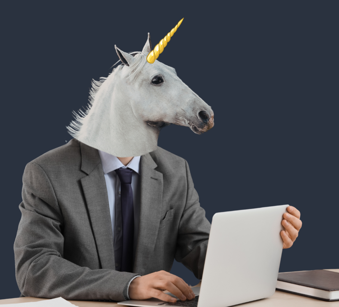 A person in a gray business suit sits at a desk using a laptop, with a marketing unicorn head with a golden horn, set against a plain dark blue background.