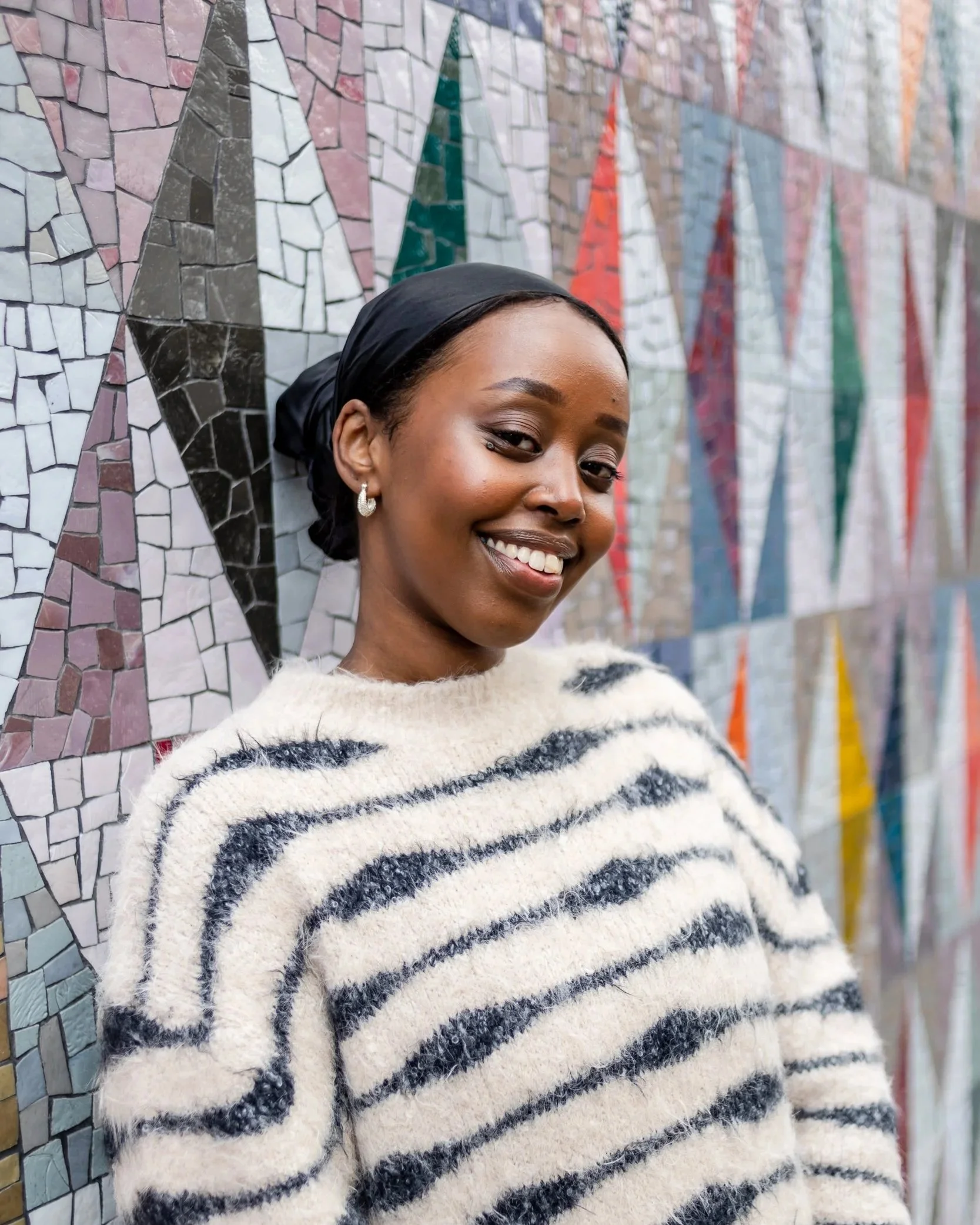 woman standing in front of a mosaic  with a stripy top smiling at the camera