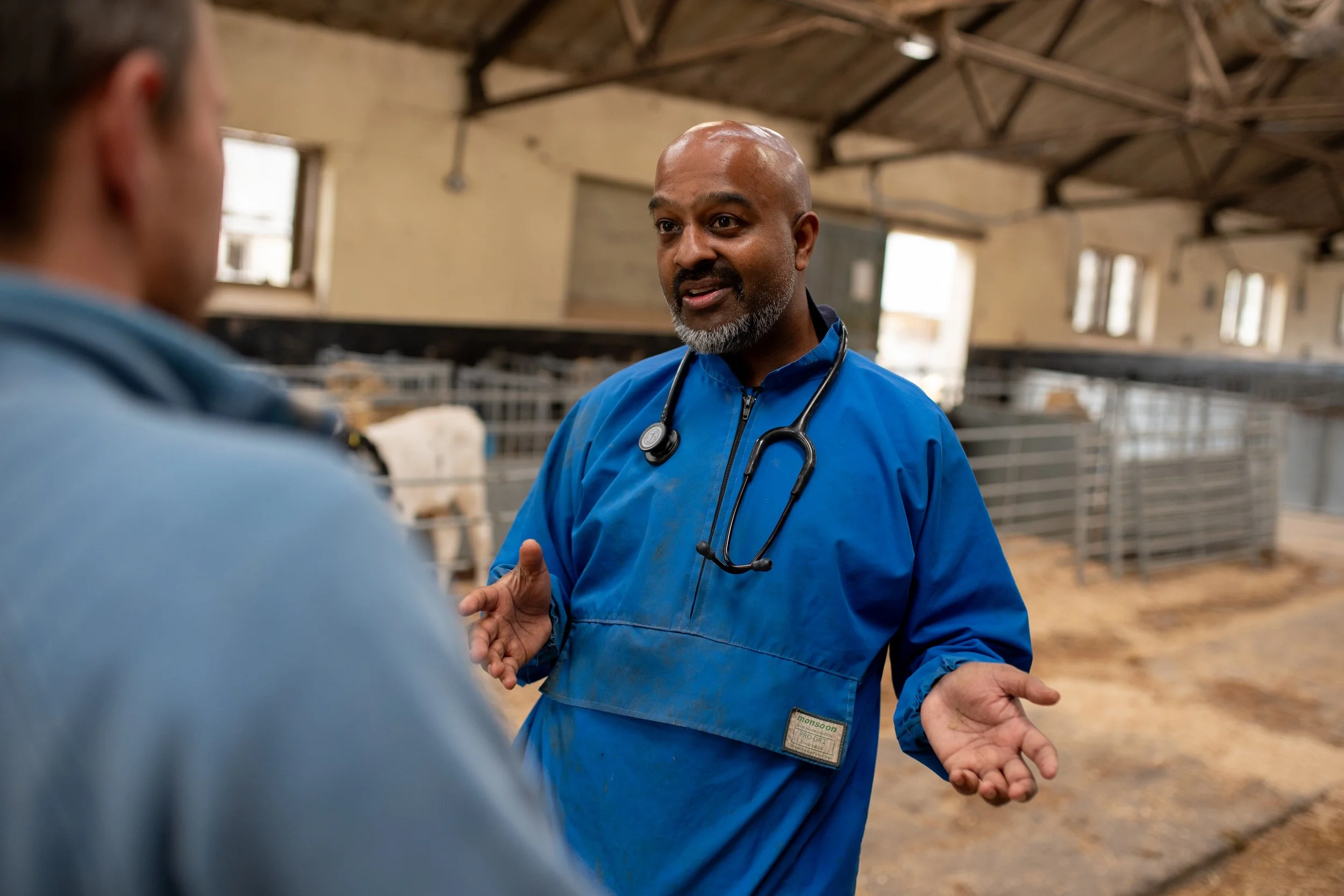Theeb having a conversation wearing vet gear (blue suit and a stethoscope), he is gesturing with his hands