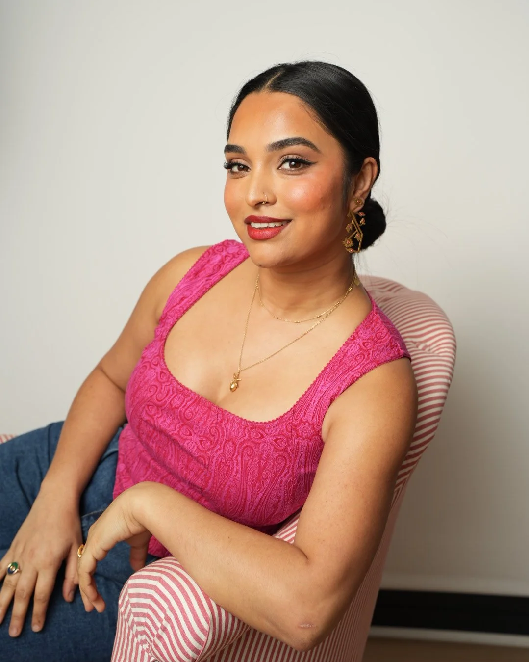 Bengali woman with hair in a bun looks at the camera, sitting on a stripy chair