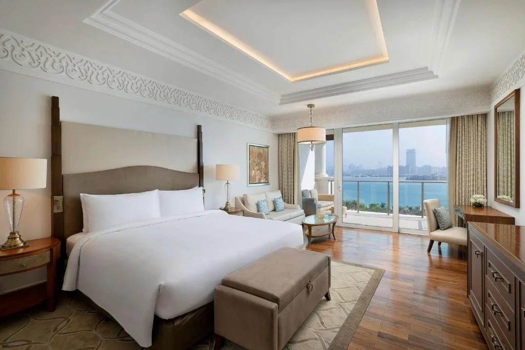 Luxurious hotel room with king-sized bed, elegant decor, and large windows overlooking a waterfront view.