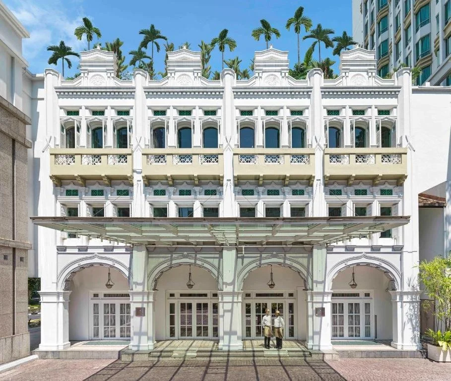 Historic colonial-style building with palm trees on the roof and two people standing at the entrance.