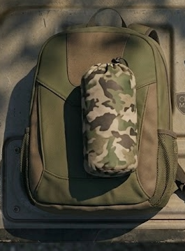 Hunting rain jacket compressed into a stuff sack sitting on a daypack next to binoculars, climbing sticks, and a saddle platform on a truck tailgate showing pack size comparison