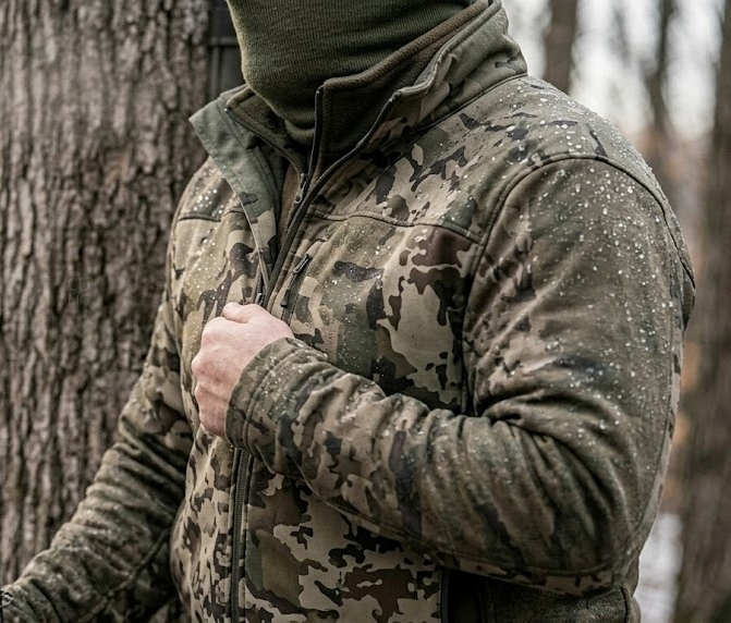 Close-up of water beading on a hunting rain jacket surface during a November rain in a treestand with rain streaks and blurred hardwood timber in the background