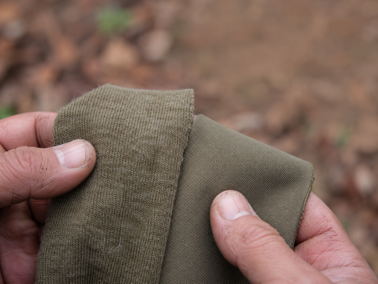 Close-up of merino wool and synthetic polyester hunting base layer fabrics held side by side showing the texture and weave difference between the two materials