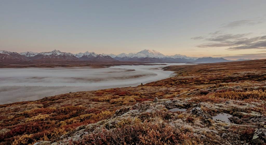 Autumn tundra bench in interior Alaska at dawn with fog in the valley and snow-capped peaks behind, classic public land hunting in Alaska caribou country during September season.