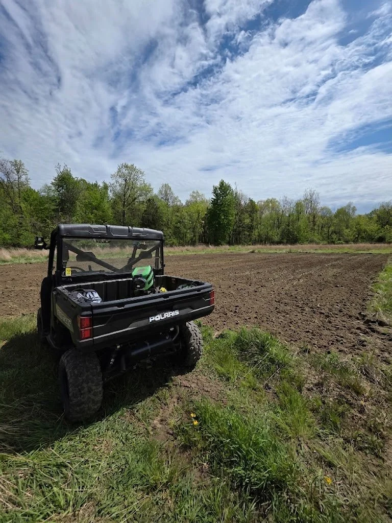 Polaris Ranger UTV parked at the edge of a freshly tilled 2.5-acre food plot in southwest Michigan with spring hardwood timber leafing out in the background and overcast sky