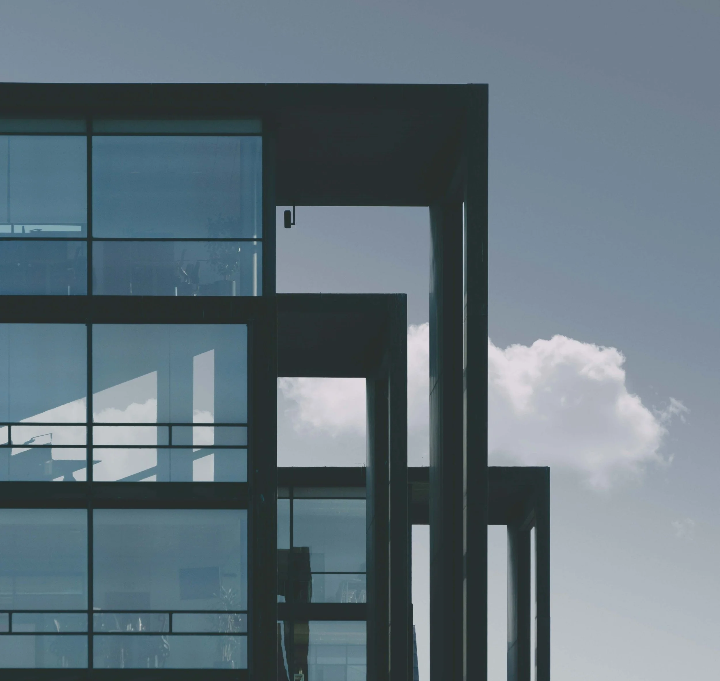 Modern building with glass walls and balcony sections against a cloudy sky.