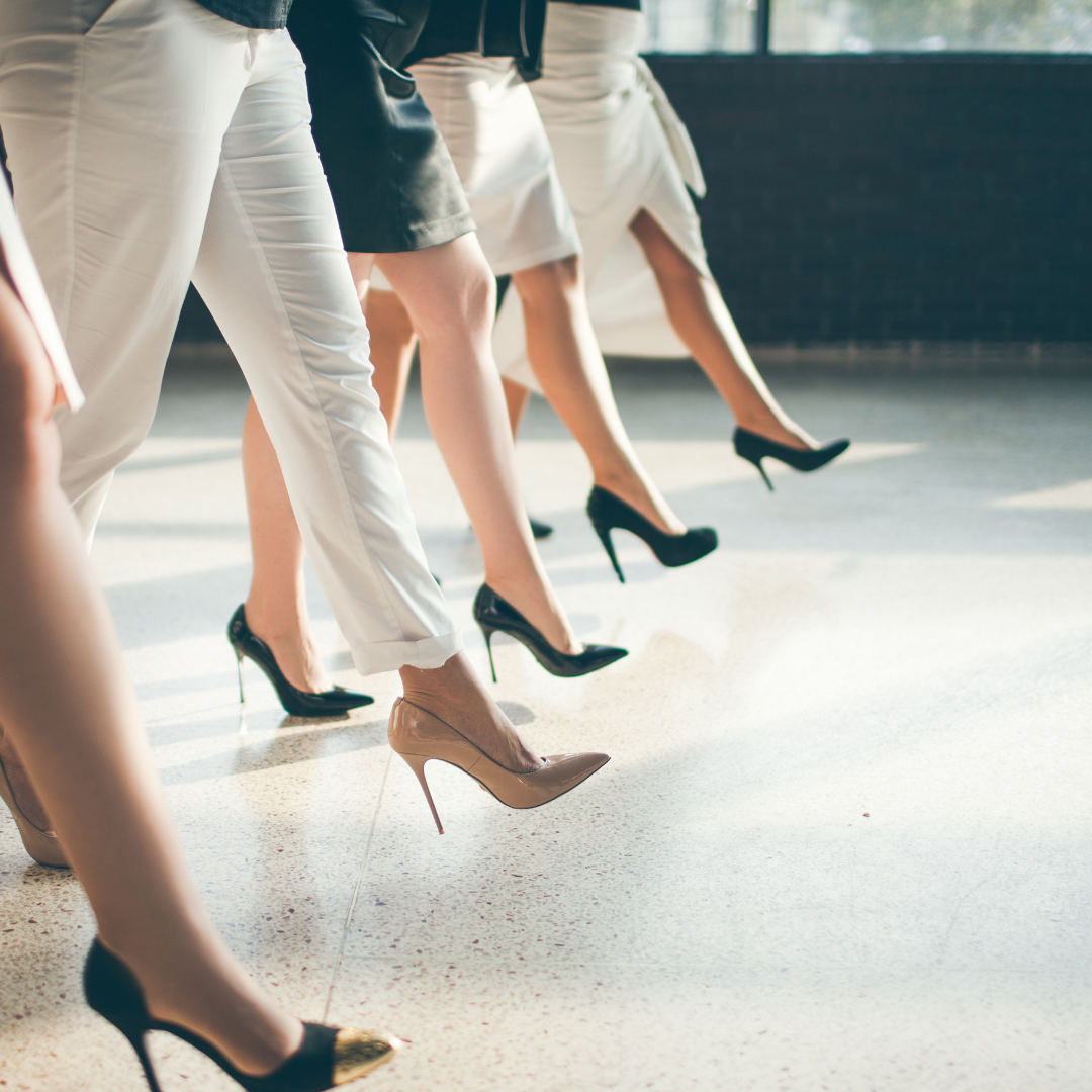 Groupe de femmes en talons hauts, portant des vêtements élégants, marchant d'un même pas dans une pièce lumineuse.