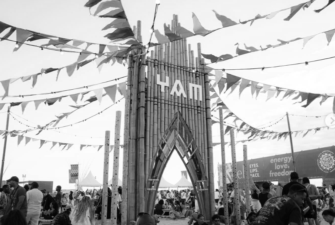 Crowd of people at outdoor festival with bamboo structure, banner reading 'YAP', and decorative flags and string lights.