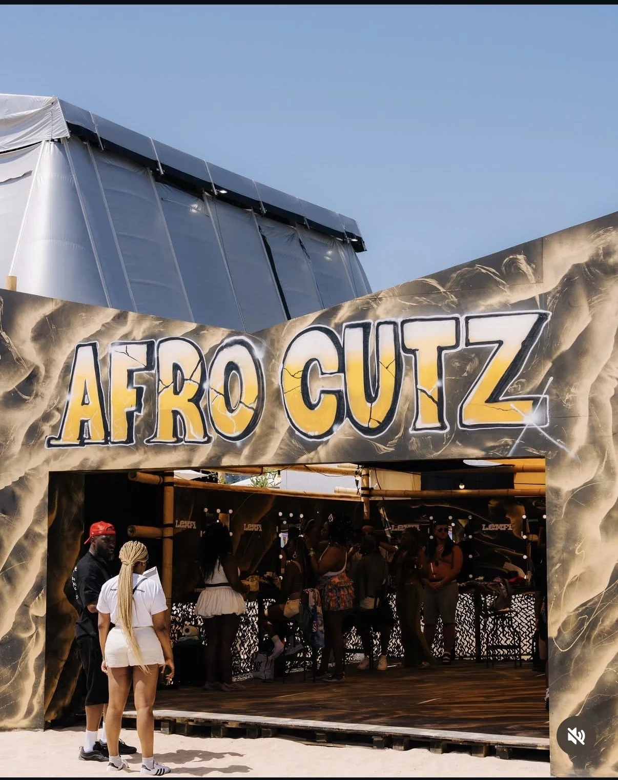 People standing outside an African-themed booth with a sign that says 'AFRO CUTZ' at an outdoor event or festival.