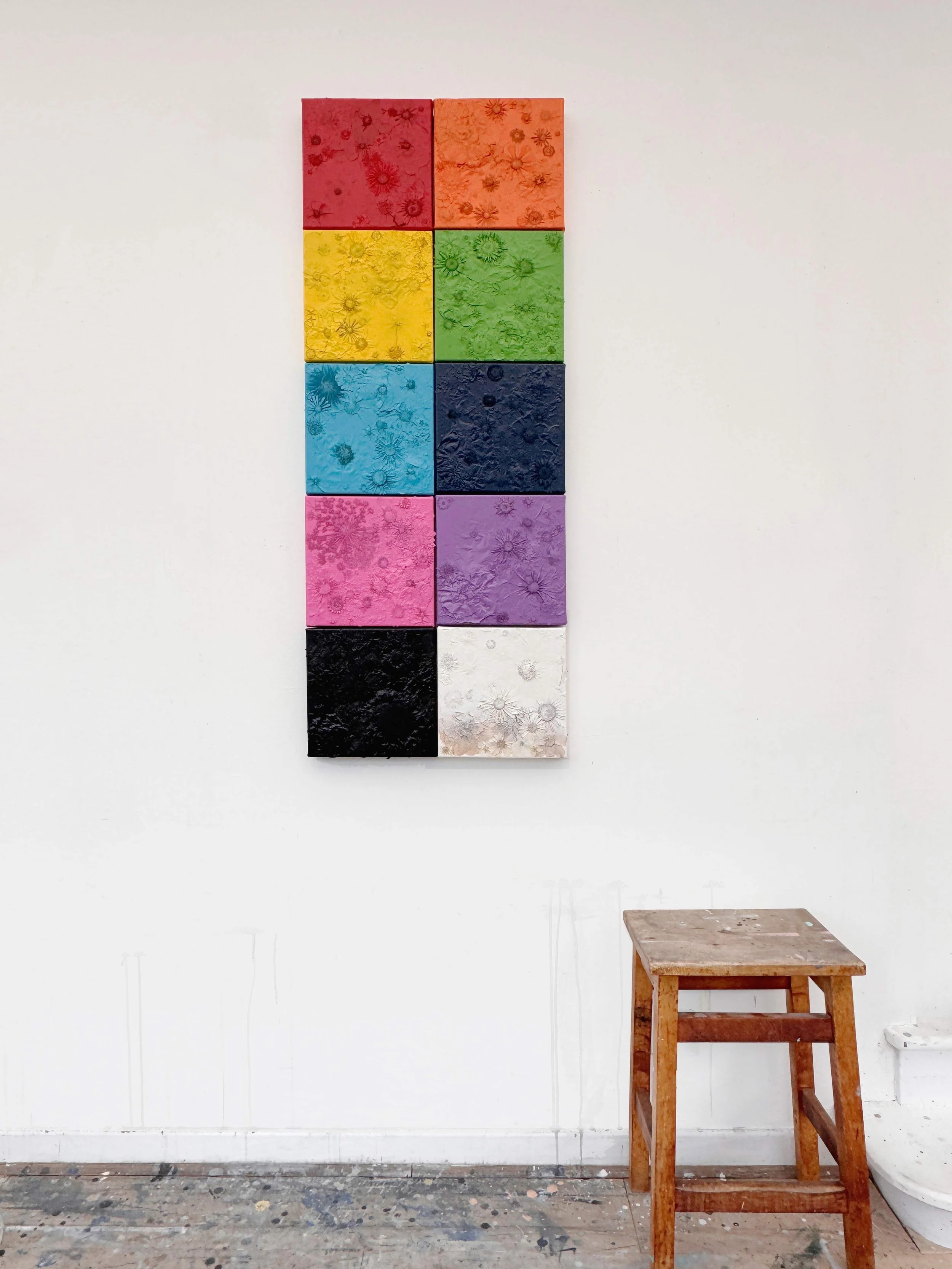 Large artwork made with pressed flowers in the shape of a human, leaning against a studio wall