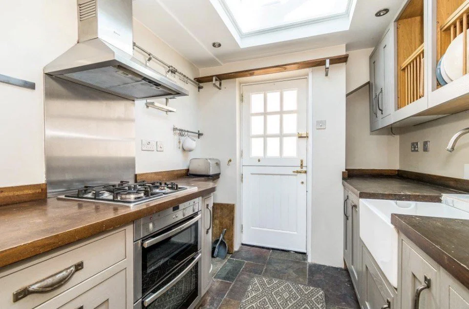 Compact kitchen with wooden countertops, gray cabinets, a gas stove, a toaster, and a white door with a window, under a skylight.