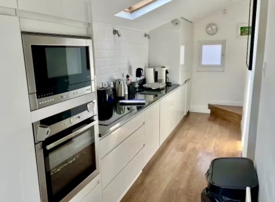 Modern kitchen with white cabinets, a black countertop, microwave, oven, coffee maker, and stone tile floor.